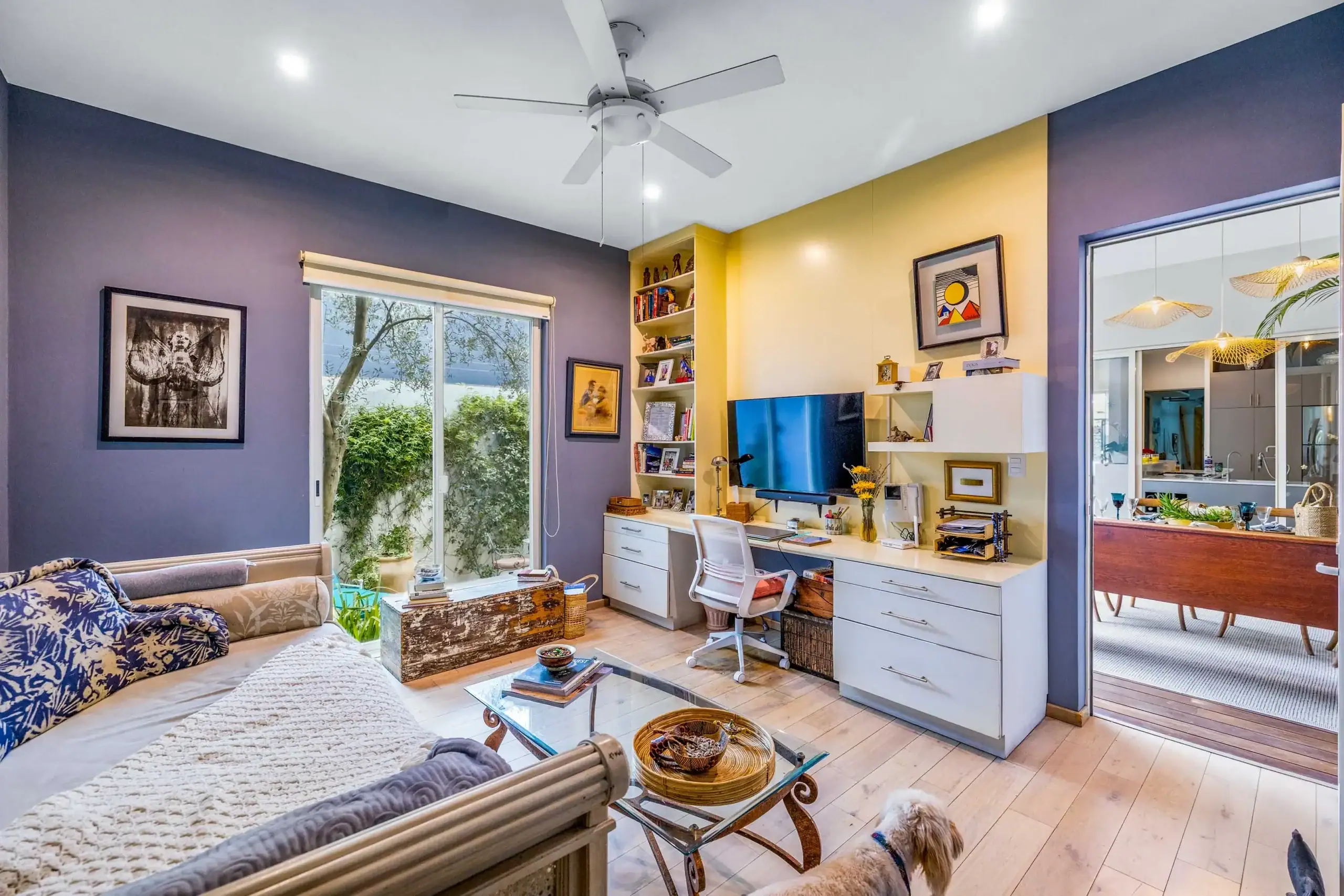 Living room with purple and yellow walls, white ceiling fan, and sliding glass door to a garden outside porch/yard, San Miguel de Allende
