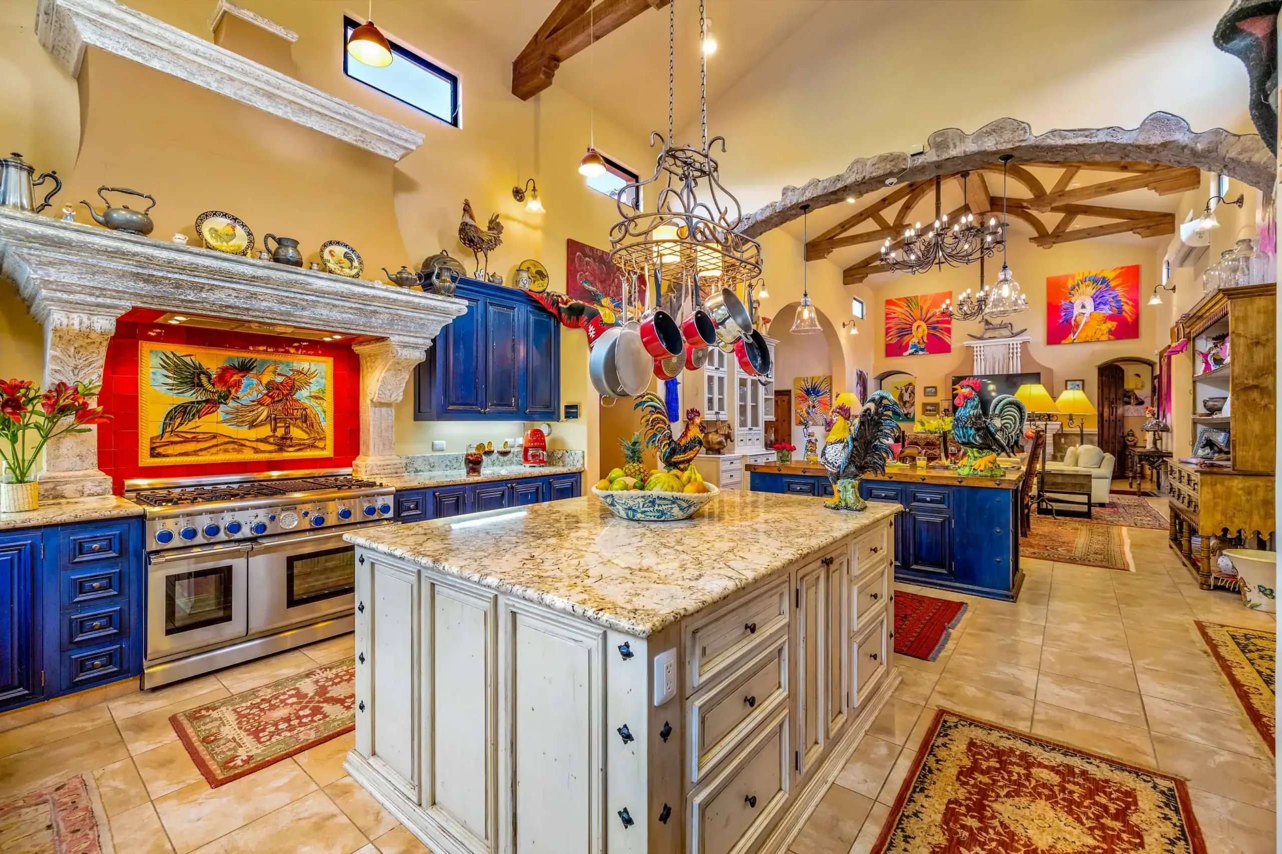 Bright kitchen with blue cabinets, marble countertops, hanging pots, and a stone mantel in a colorful, art-filled space, San Miguel de Allende