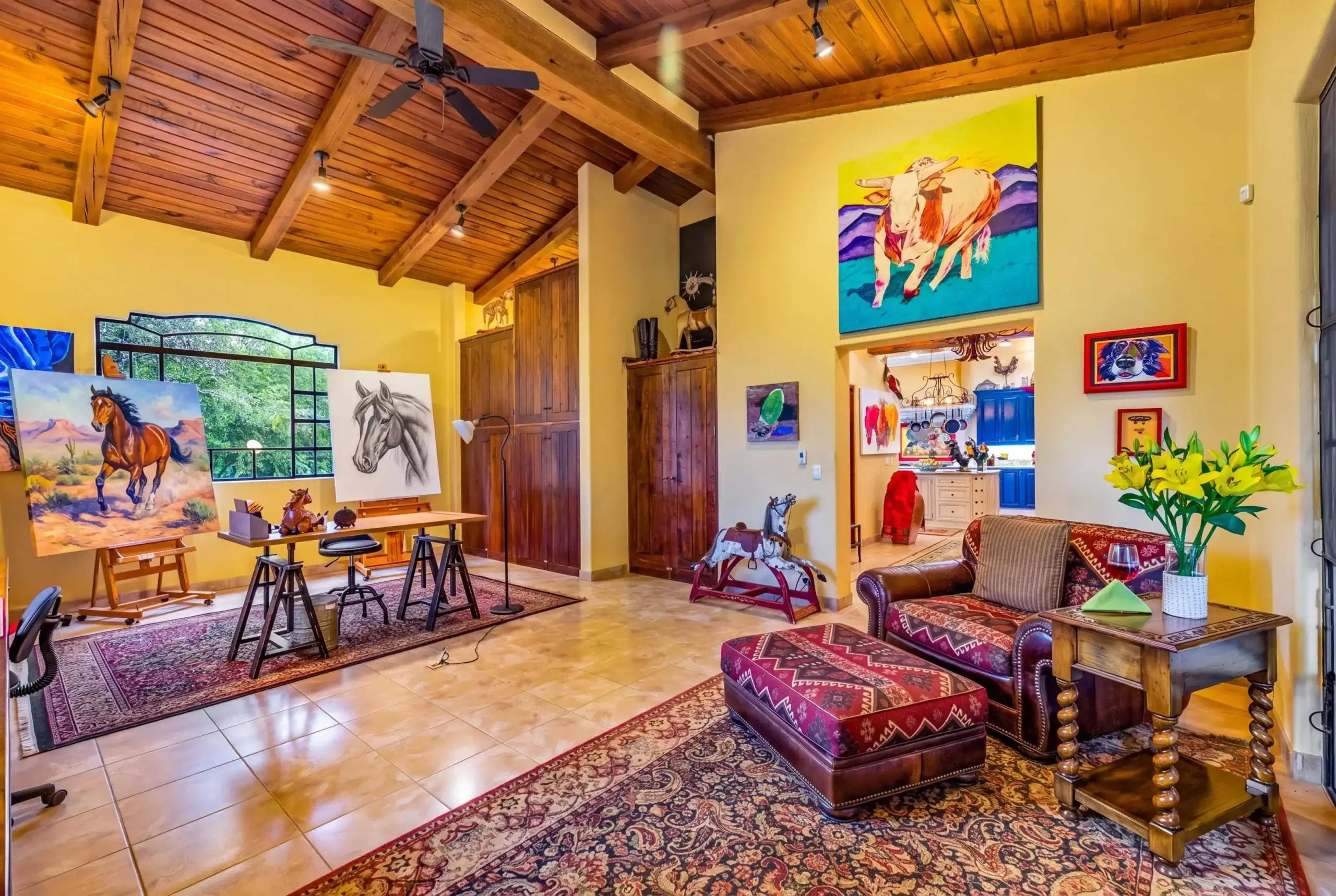 Bright artist studio with yellow walls, wooden vaulted ceiling, and horse paintings on easels, San Miguel de Allende
