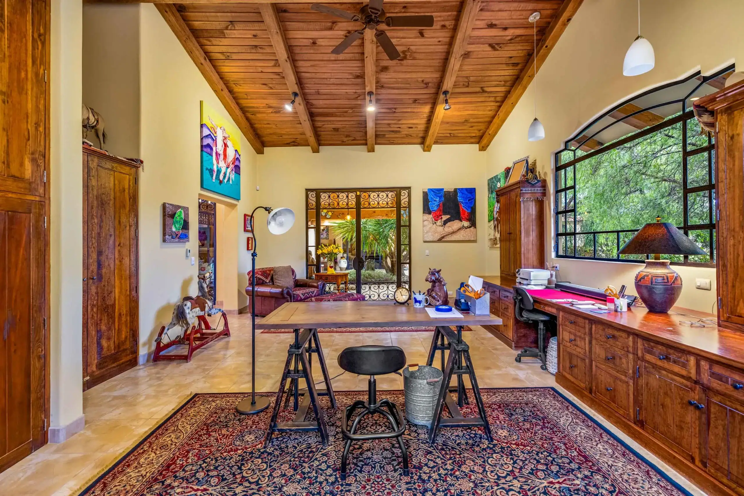 Home office with a vaulted wooden ceiling, large arched window, and a cluttered desk surrounded by painted walls and cabinets, San Miguel de Allende