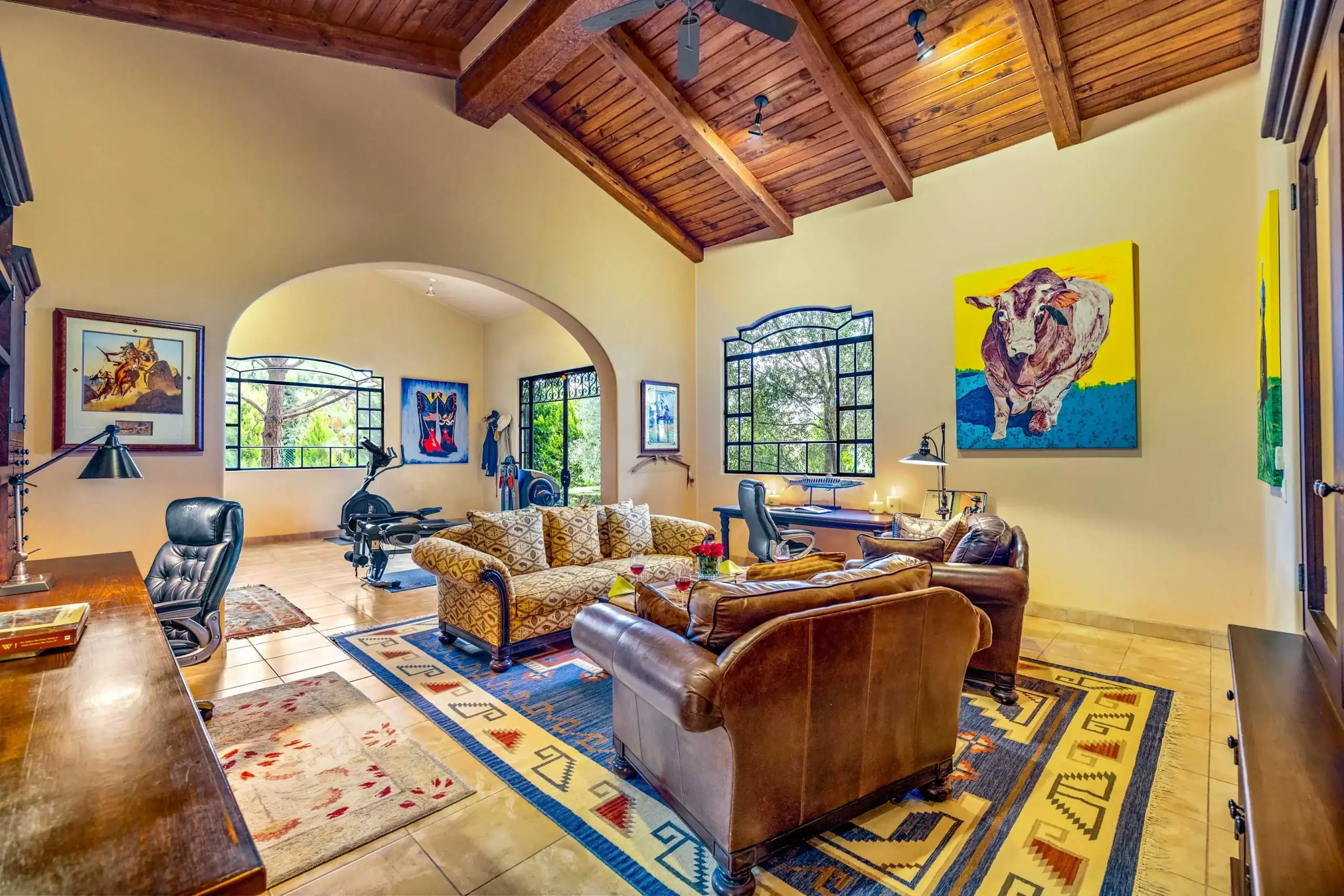 Cozy living room with a vaulted wooden beam ceiling, leather sofas, and colorful wall art; large arched windows let in light, San Miguel de Allende