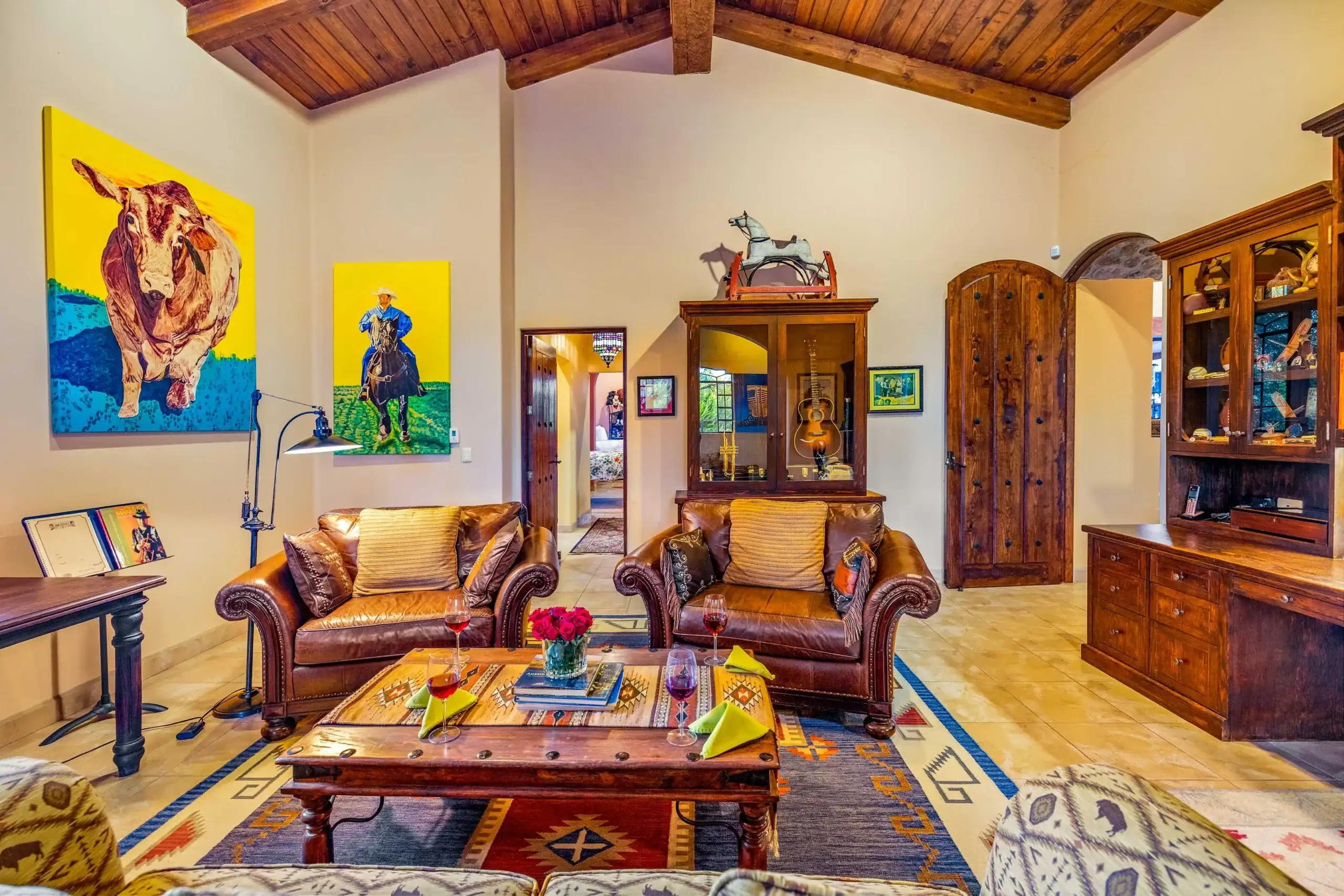 Cozy living room with brown leather sofas, a wooden coffee table, colorful art on the walls, and rustic ceiling beams, San Miguel de Allende