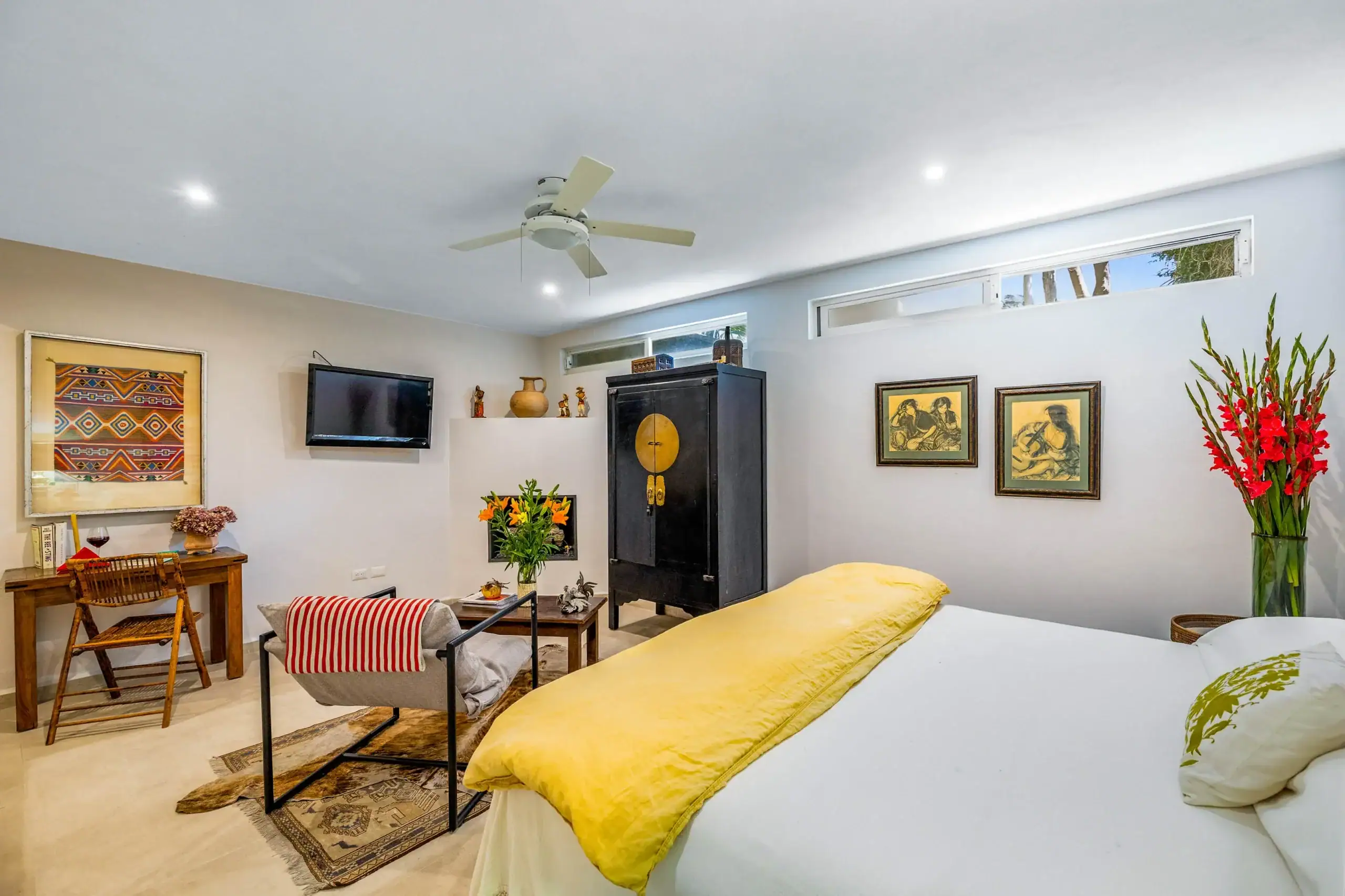 Living room–bedroom combo: two beds with yellow comforters, a small seating area, and a wall-mounted TV above a wooden desk, San Miguel de Allende