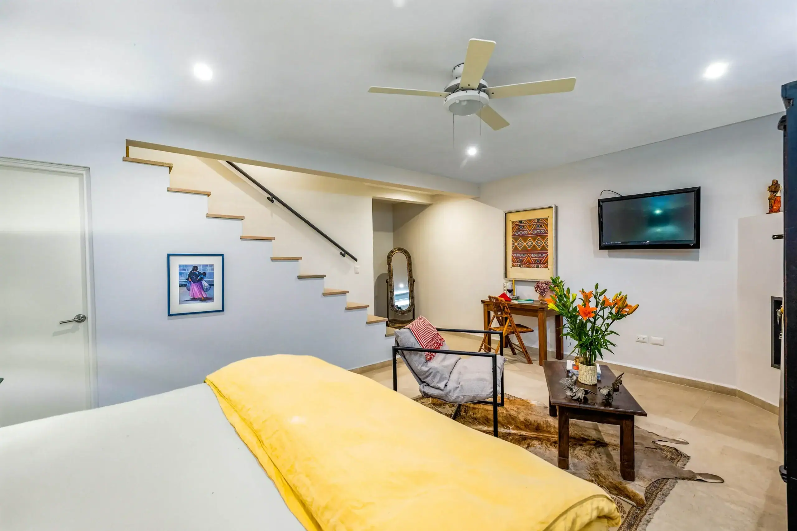 Living room with a white staircase on the left, ceiling fan overhead, and a wall-mounted TV with framed art nearby, San Miguel de Allende