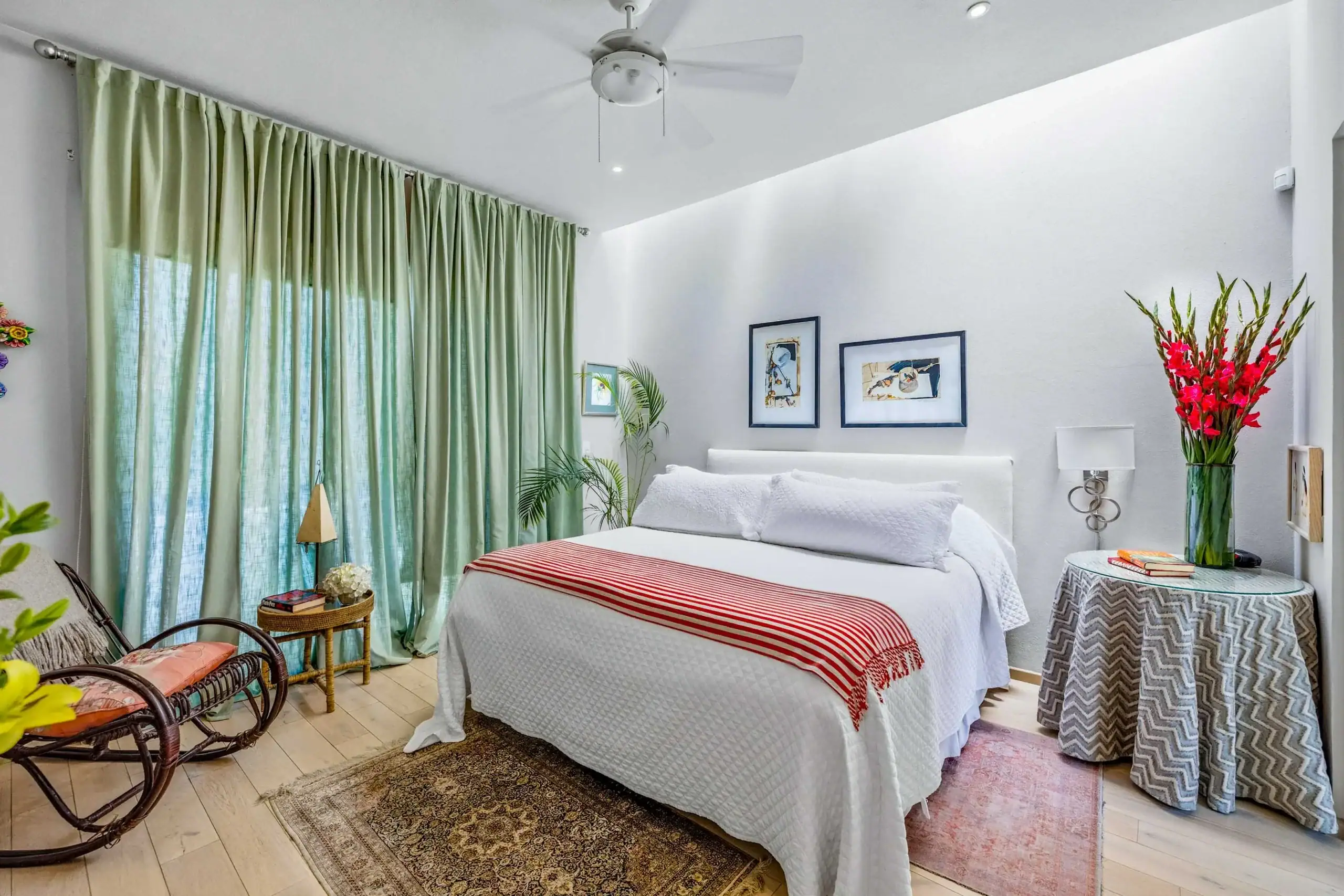 Bright bedroom with white bedding, red-striped throw, and mint-green curtains; potted plants and wall art enhance the space, San Miguel de Allende
