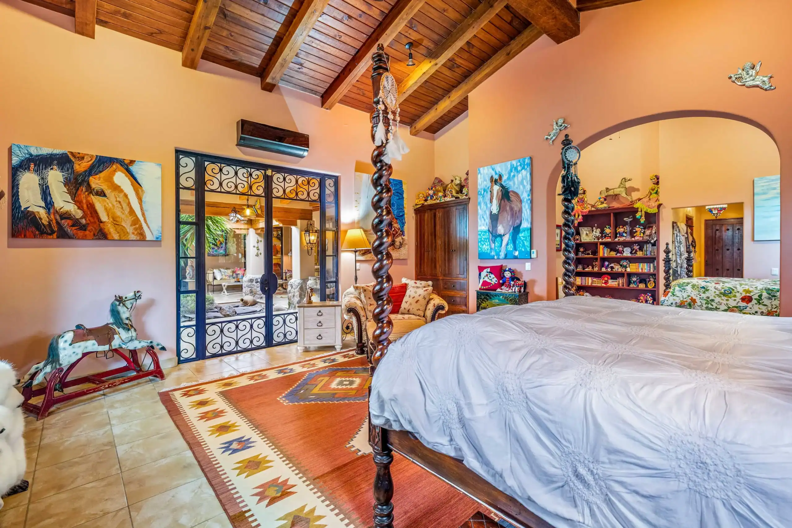 Bedroom with orange walls, wood-beam ceiling, and two ornate four-poster beds, San Miguel de Allende