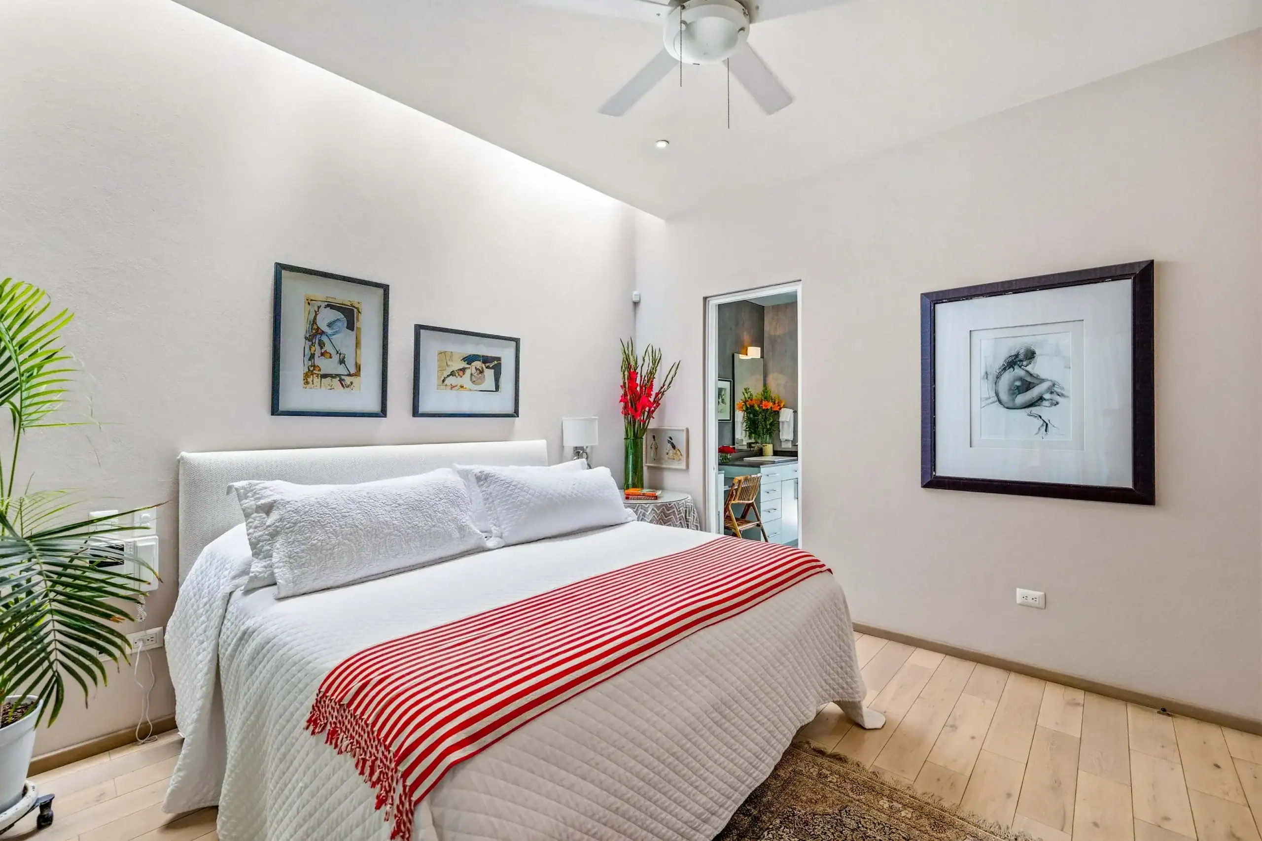Bright modern bedroom with a white quilted bed, red-striped throw, and framed wall art above the headboard, San Miguel de Allende
