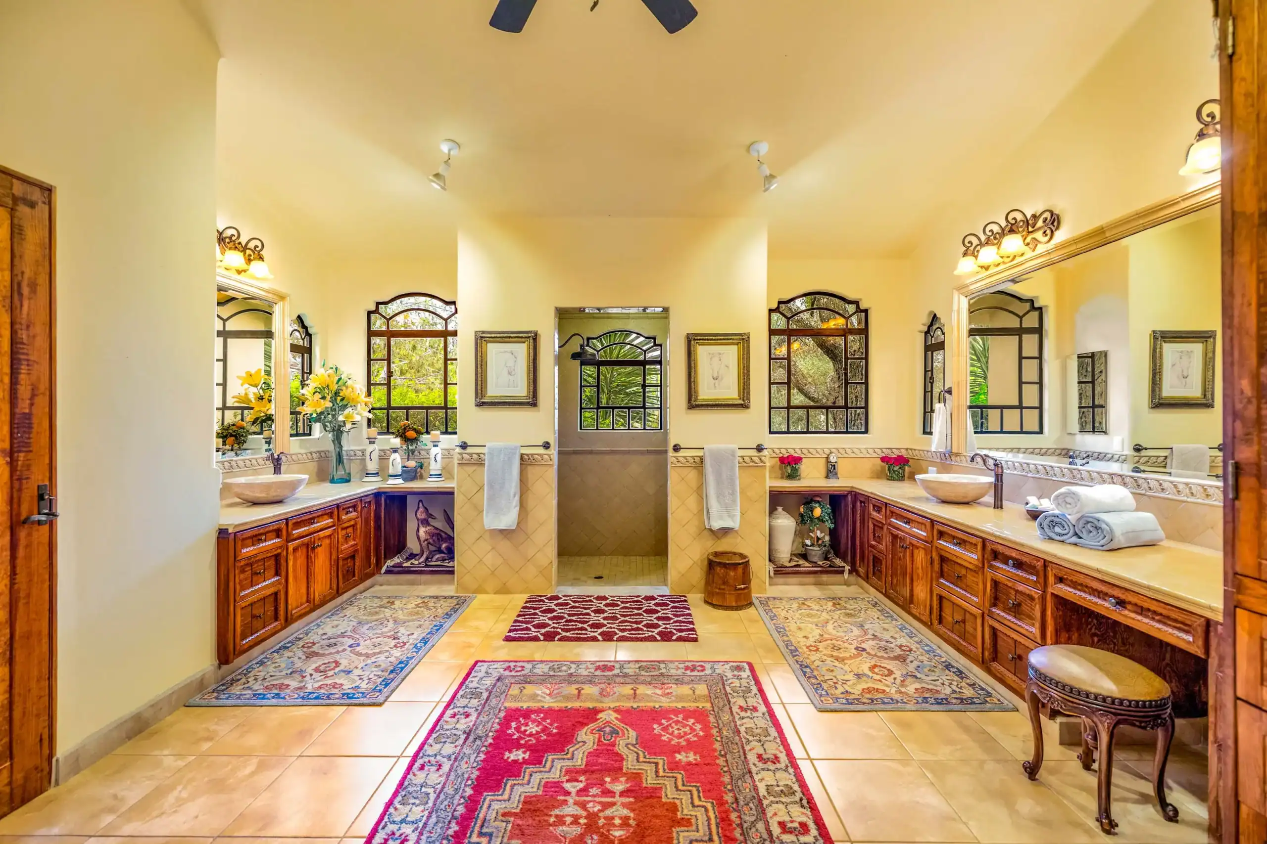 Luxurious master bathroom with double sinks, wood cabinetry, framed mirrors, and colorful area rugs, San Miguel de Allende