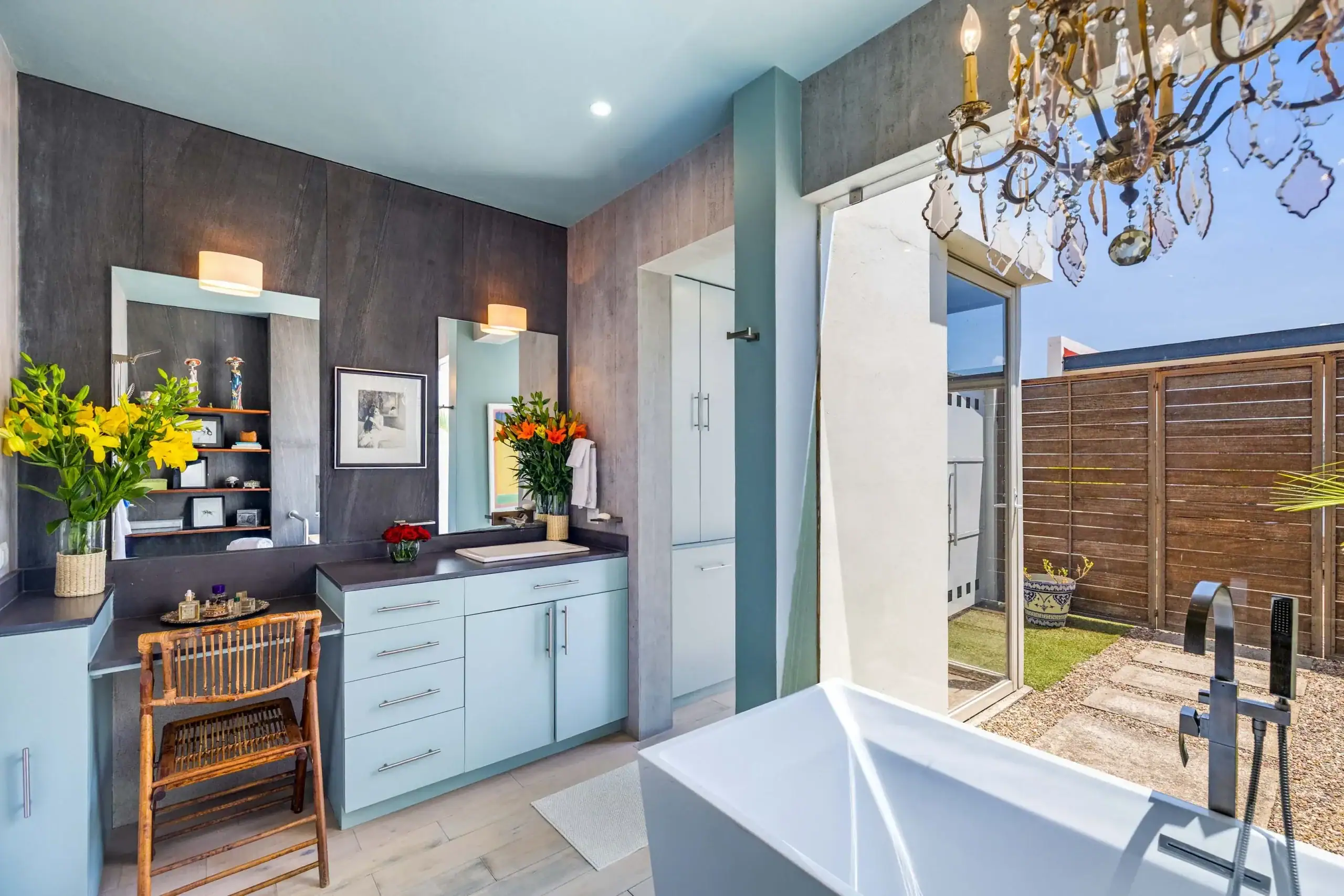 Modern bathroom with blue cabinetry, gray walls, and large mirrors reflecting a vase of yellow flowers on the counter, San Miguel de Allende