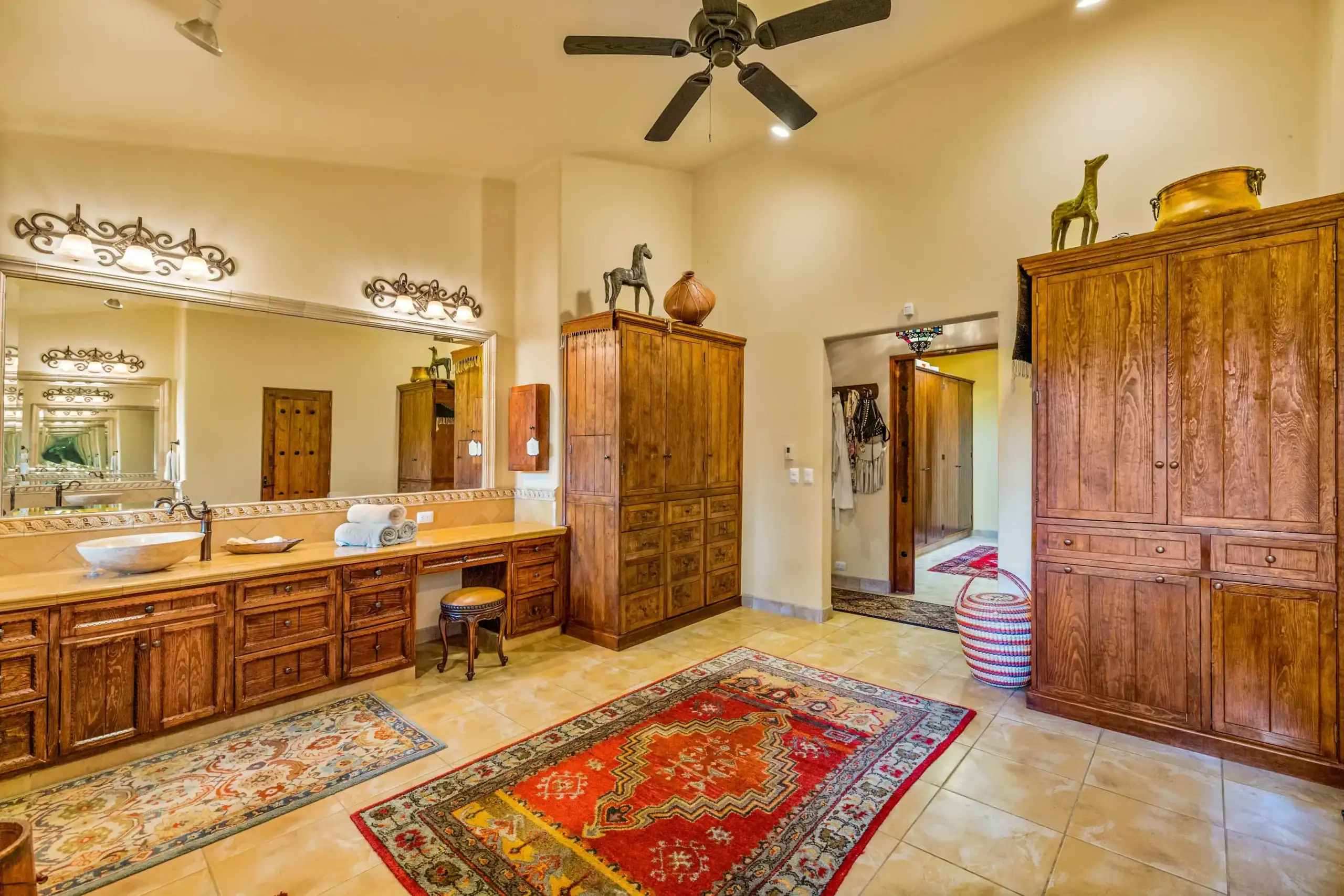 Wooden vanity and tall cabinets line a beige-walled dressing area, topped with decorative horse sculptures and pottery; colorful oriental rugs cover tiled floor, San Miguel de Allende
