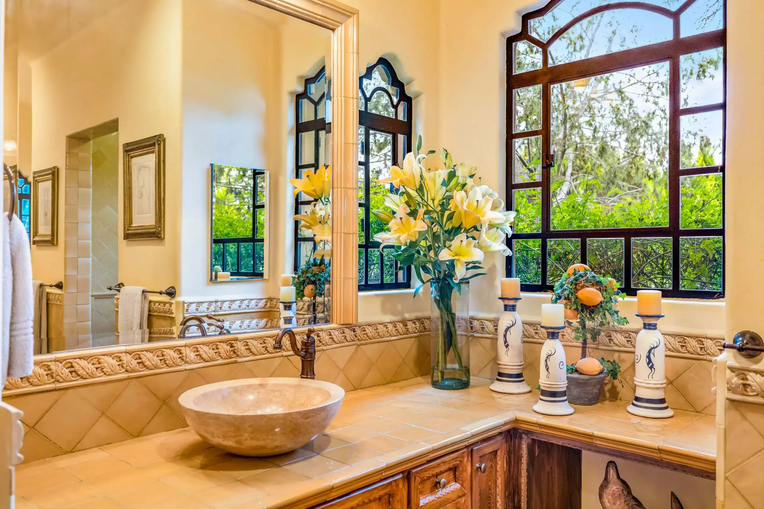 Luxurious bathroom vanity with beige tiles, a marble bowl sink, and large arched windows overlooking greenery, San Miguel de Allende