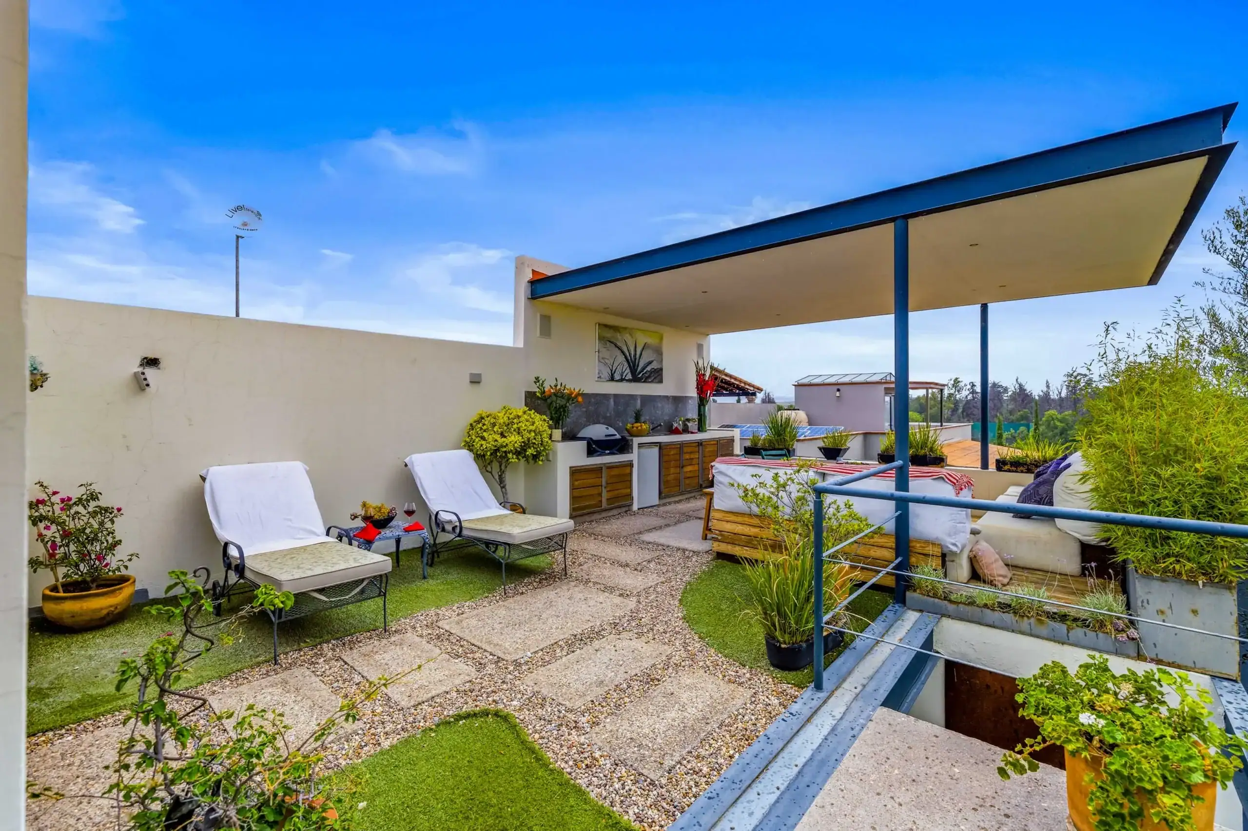 Rooftop terrace with white-cushioned chairs, potted plants, and a long countertop under a blue canopy against a clear sky, San Miguel de Allende