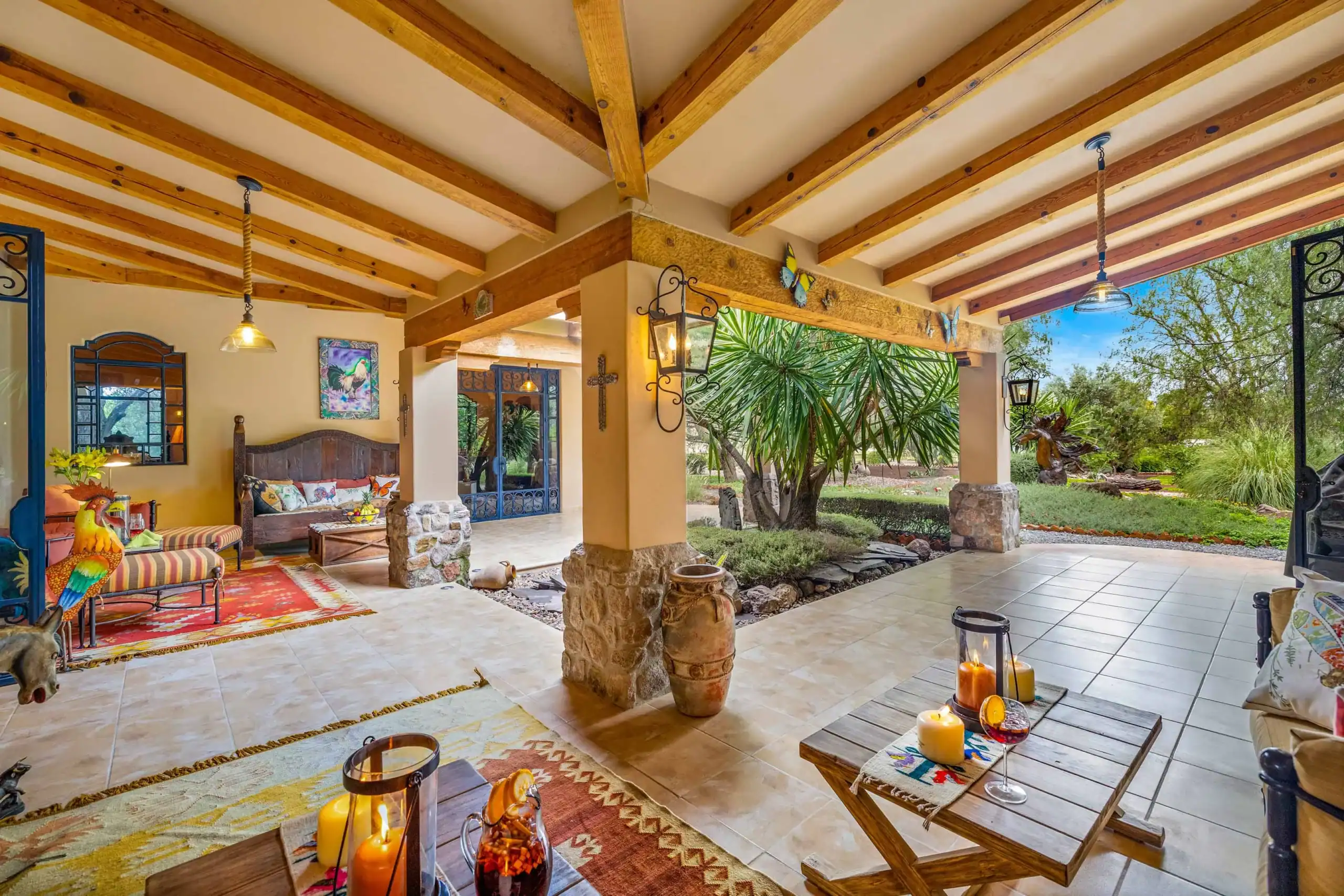 Covered patio with exposed wooden beams, stone columns, and cozy seating; garden visible outside with plants and trees, San Miguel de Allende