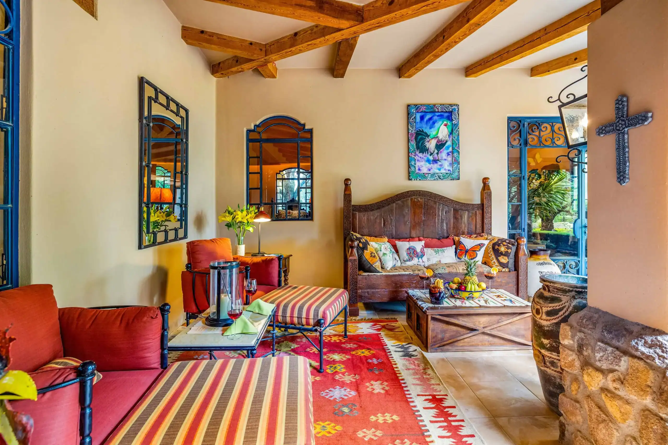 Cozy living room with red-stripe upholstered seating, a carved wooden sofa, colorful rug, and exposed wood beams on the ceiling, San Miguel de Allende