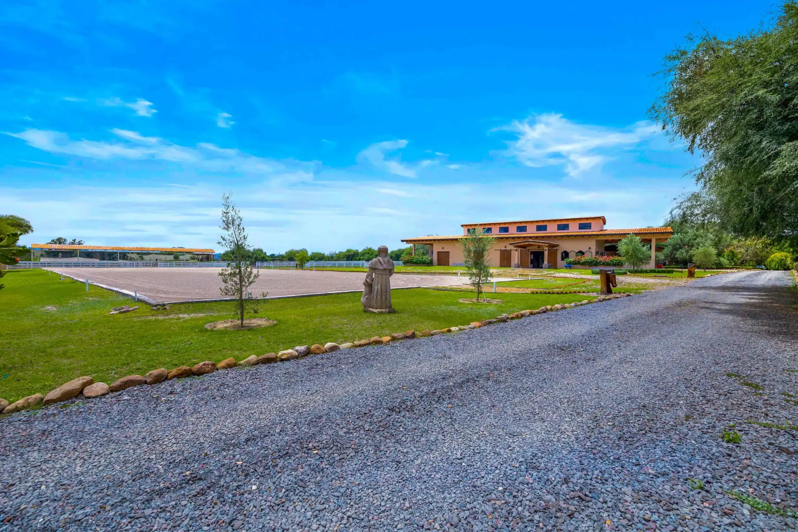 Rural estate with a peach-colored building, statue in the front yard, gravel driveway, and expansive blue sky above, San Miguel de Allende