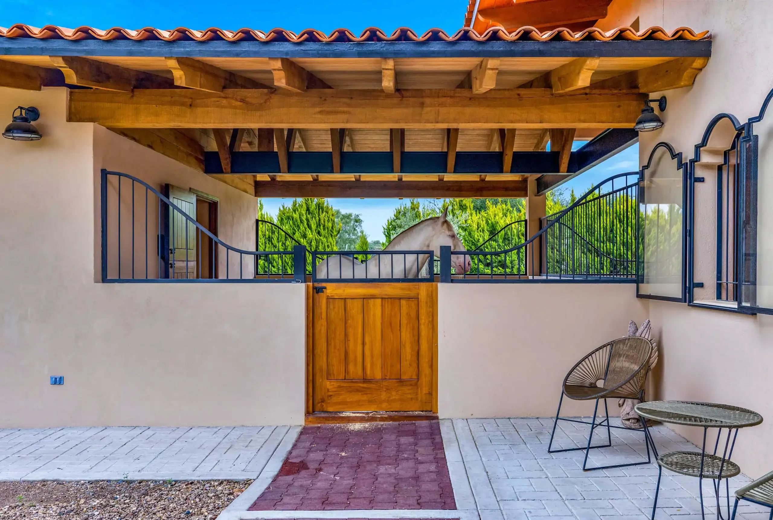 Wide-angle view of a stucco courtyard with a wooden door, iron gate, and exposed wooden beams; a white horse stands behind the gate, San Miguel de Allende