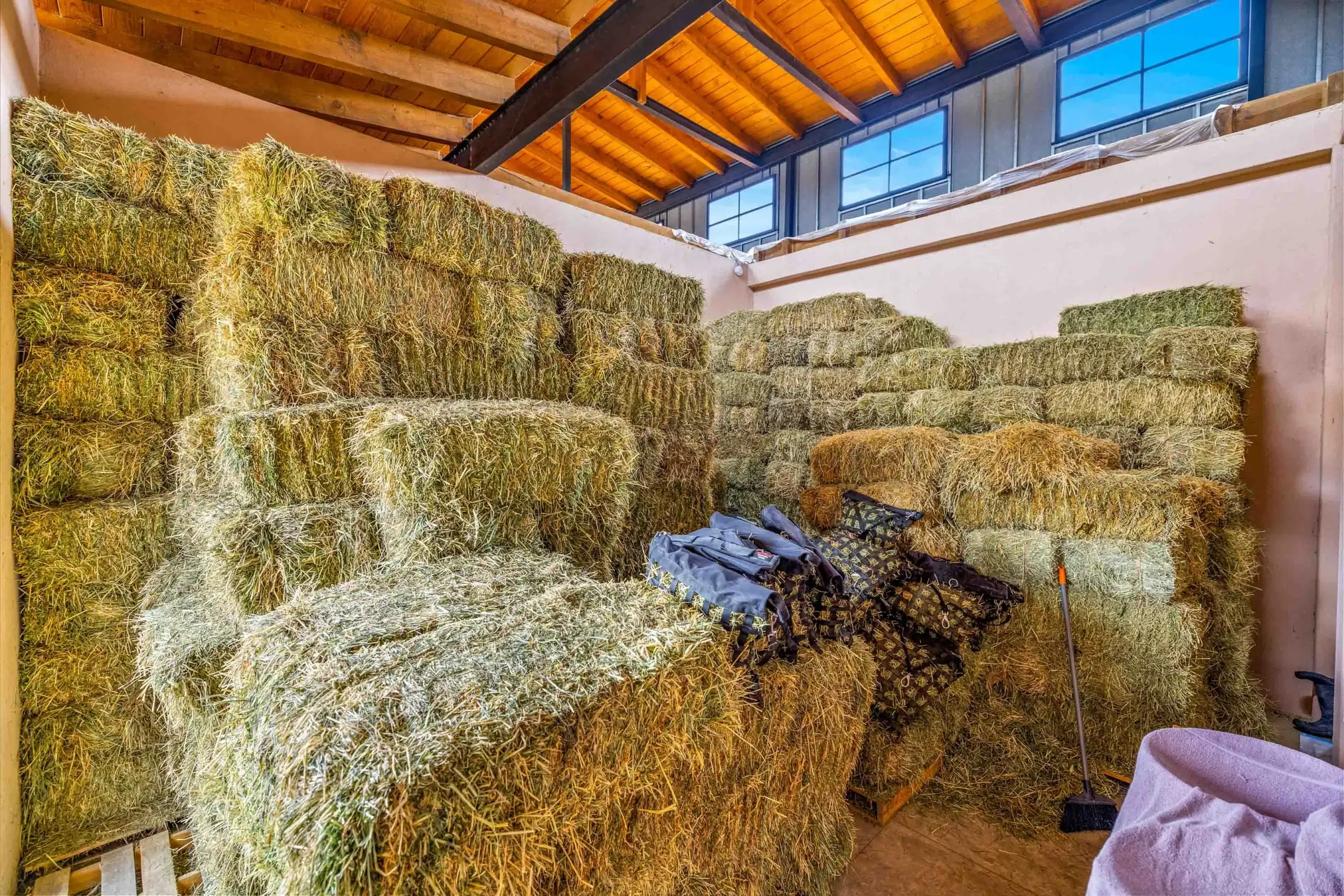 Stacks of hay bales piled high in a barn under wooden beams and large windows, San Miguel de Allende