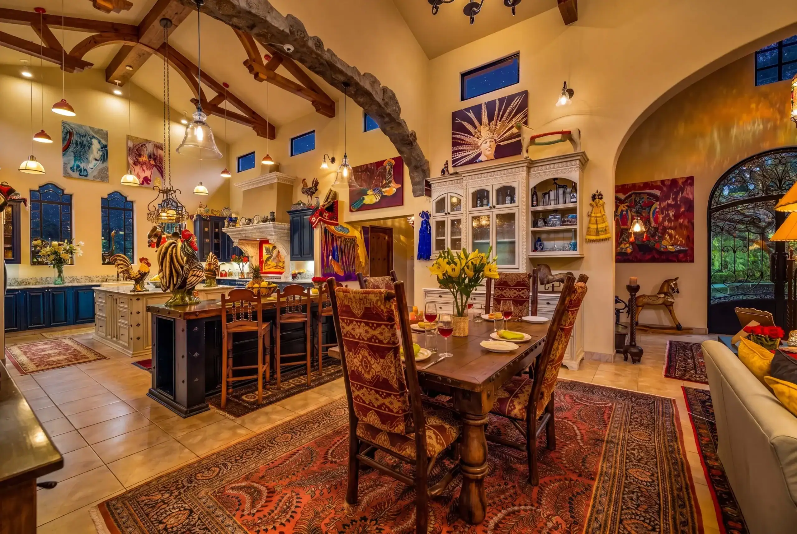 Colorful dining room with exposed wooden beams, pendant lights, and a long wooden table set for dinner with flowers and wine glasses, San Miguel de Allende