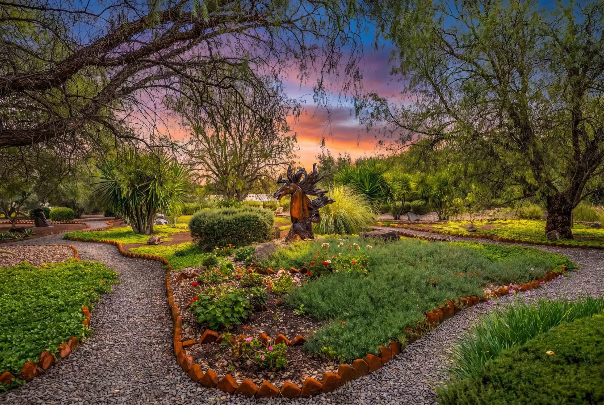 Sunset garden with winding gravel paths, brick borders, and a bronze sculpture framed by trees, San Miguel de Allende