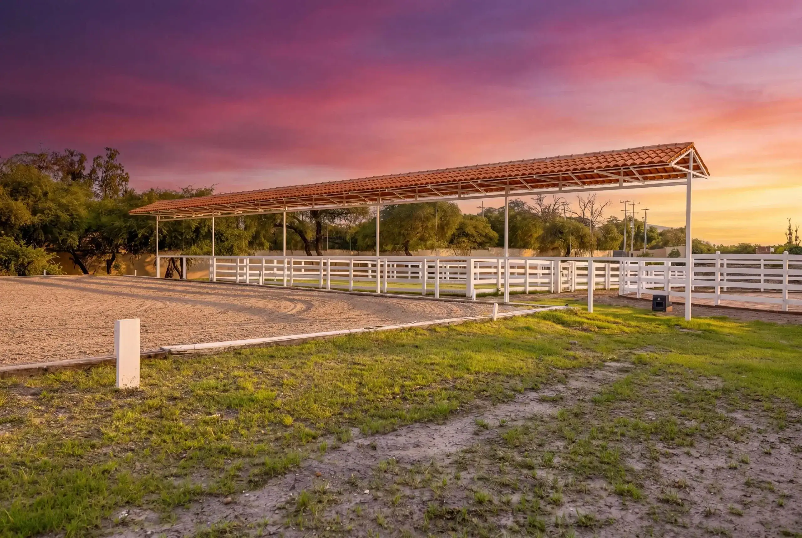 Open-air horse arena with a white fence and red-tiled shelter at sunset, San Miguel de Allende