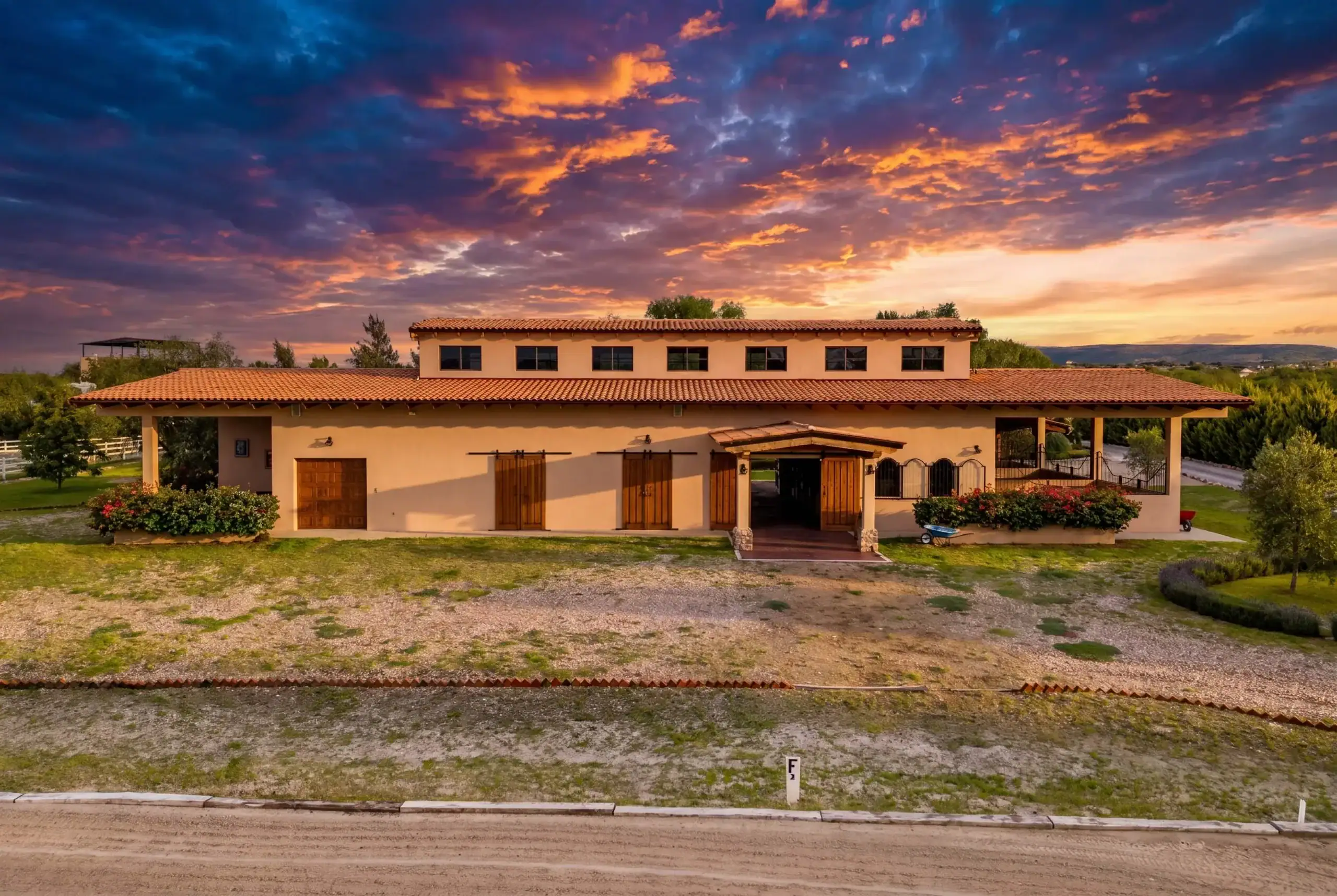 Villa-style building with a terracotta roof under a dramatic sunset sky, surrounded by greenery on a clear evening, San Miguel de Allende