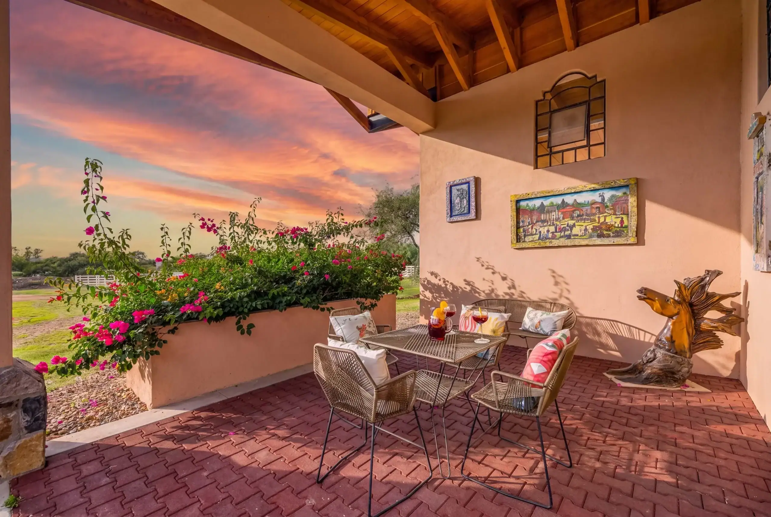 Outdoor patio with a metal table and chairs, pink flowers along a stucco wall at sunset2- patio scene with sunset sky and flowering bushes, San Miguel de Allende