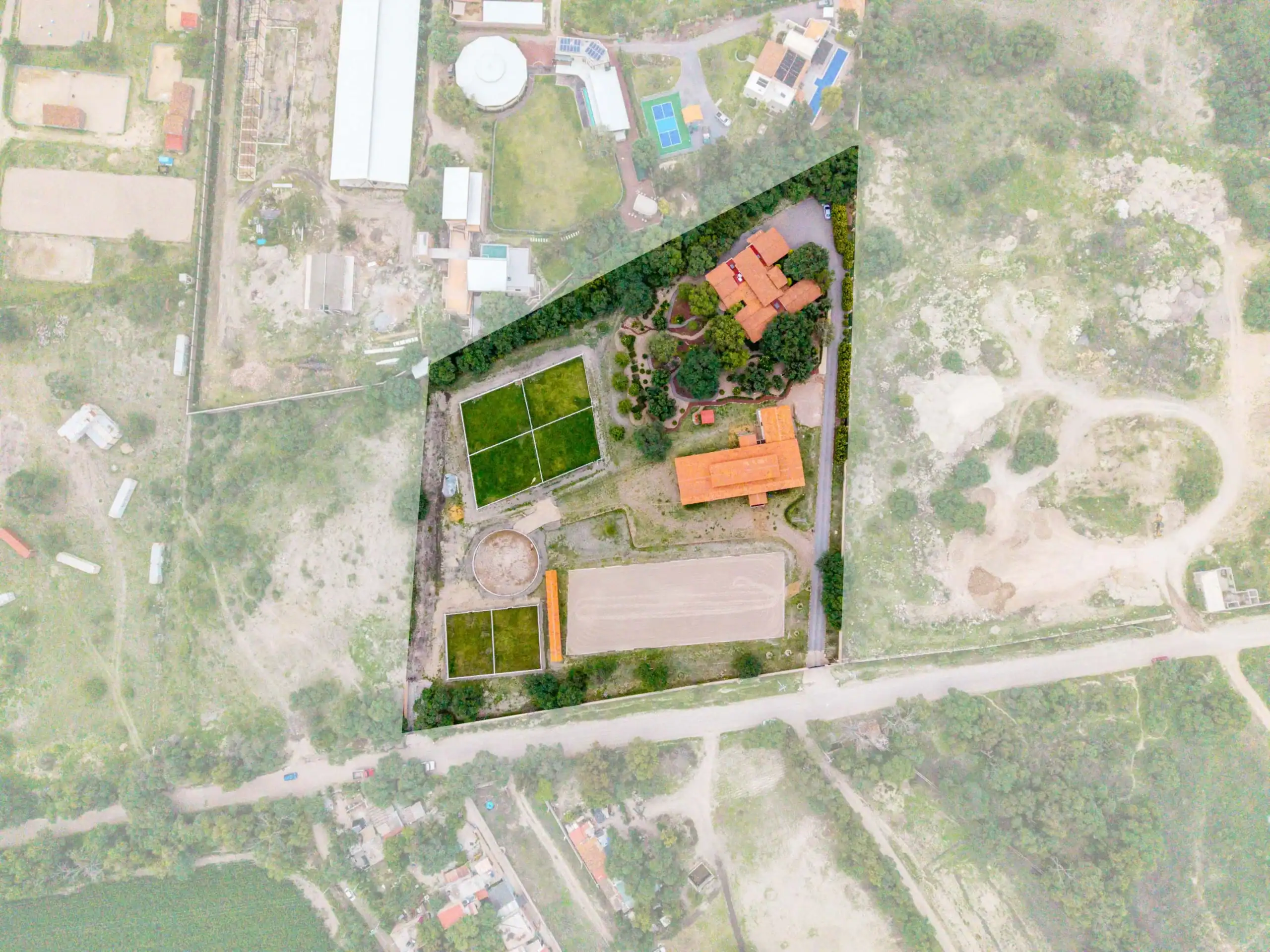 Aerial view of a campus with orange-roofed buildings, tennis court, and green spaces; a diagonal translucent overlay crosses the center, San Miguel de Allende