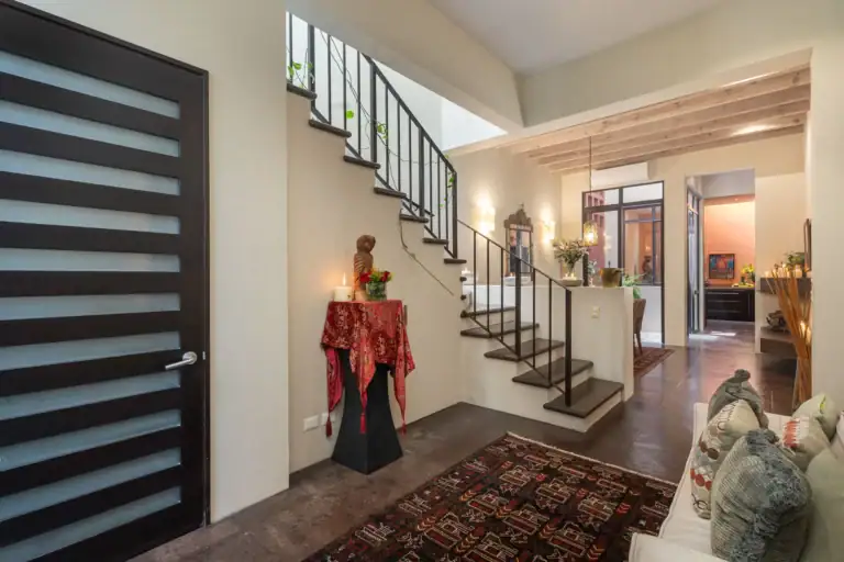 Interior of a modern home featuring a staircase with dark railing, open living area, and decorative rug runner, San Miguel de Allende
