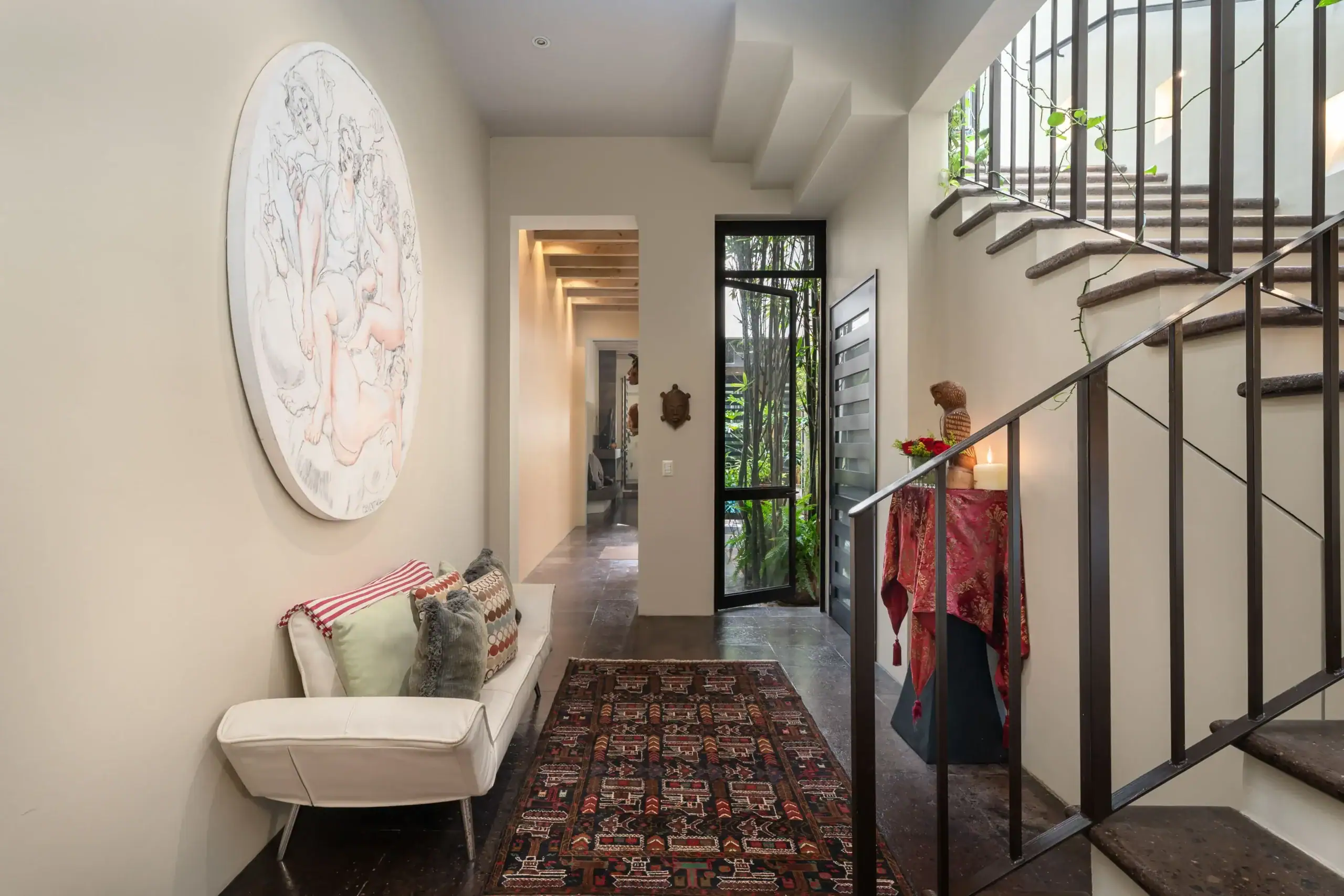Contemporary hallway with a curved metal staircase railing on the right, a round wall sculpture on the left, and a patterned rug, San Miguel de Allende