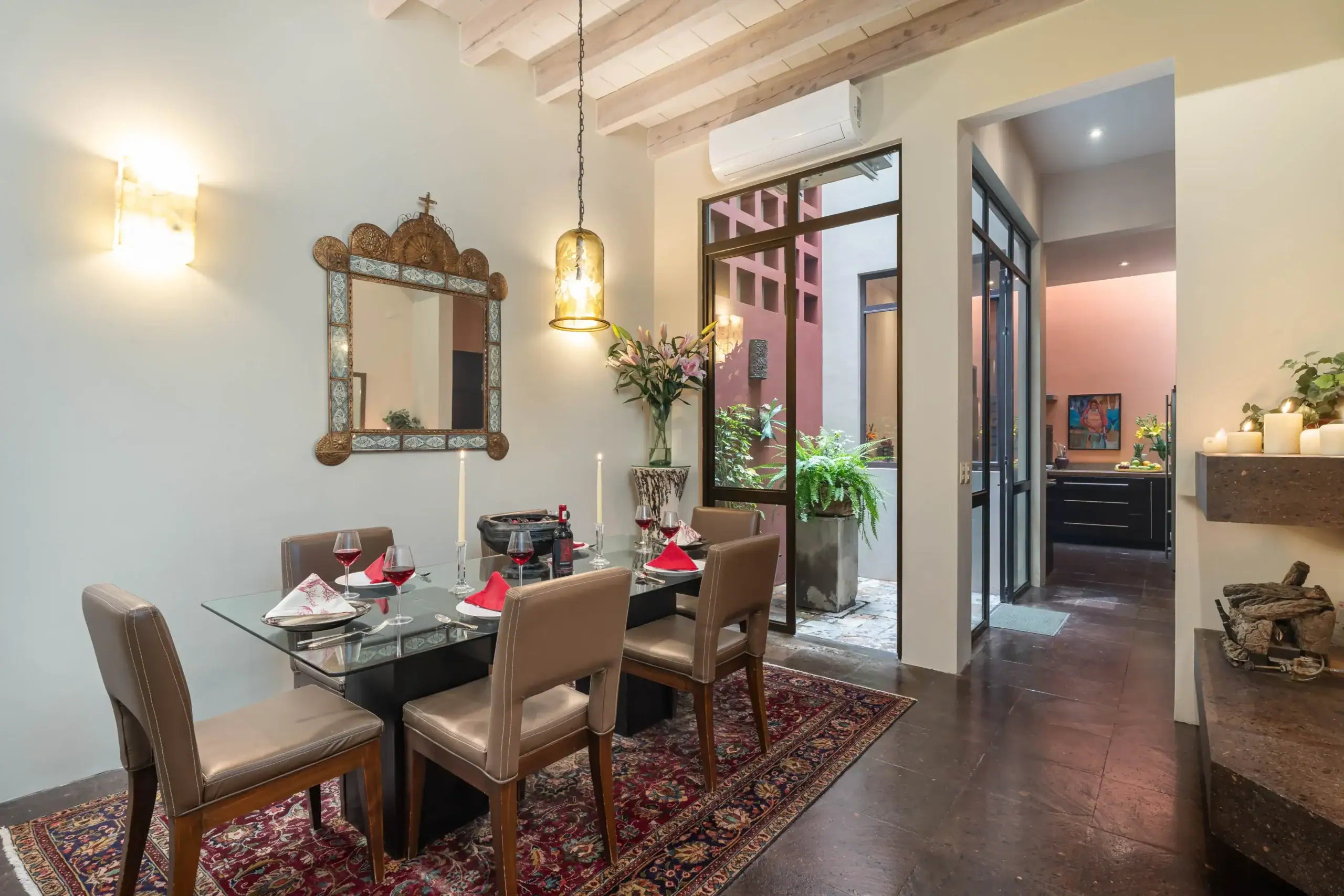 Elegant dining room with a glass-top table set for six, beige chairs, red napkins, and candles; ornate wall mirror nearby, San Miguel de Allende