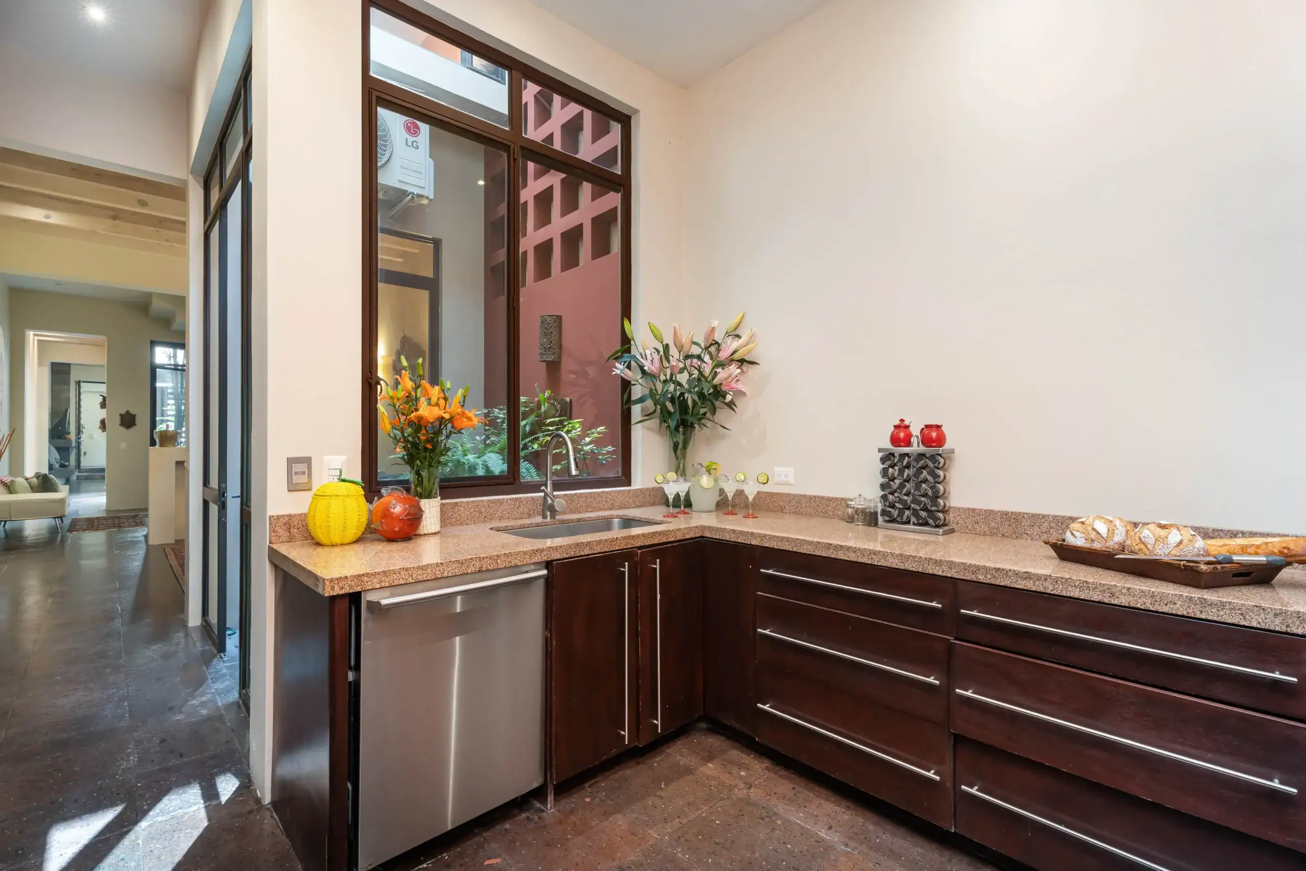 Modern kitchen with dark wood cabinets, granite countertops, and a large window over the sink; flowers and fruit décor on the counter, San Miguel de Allende