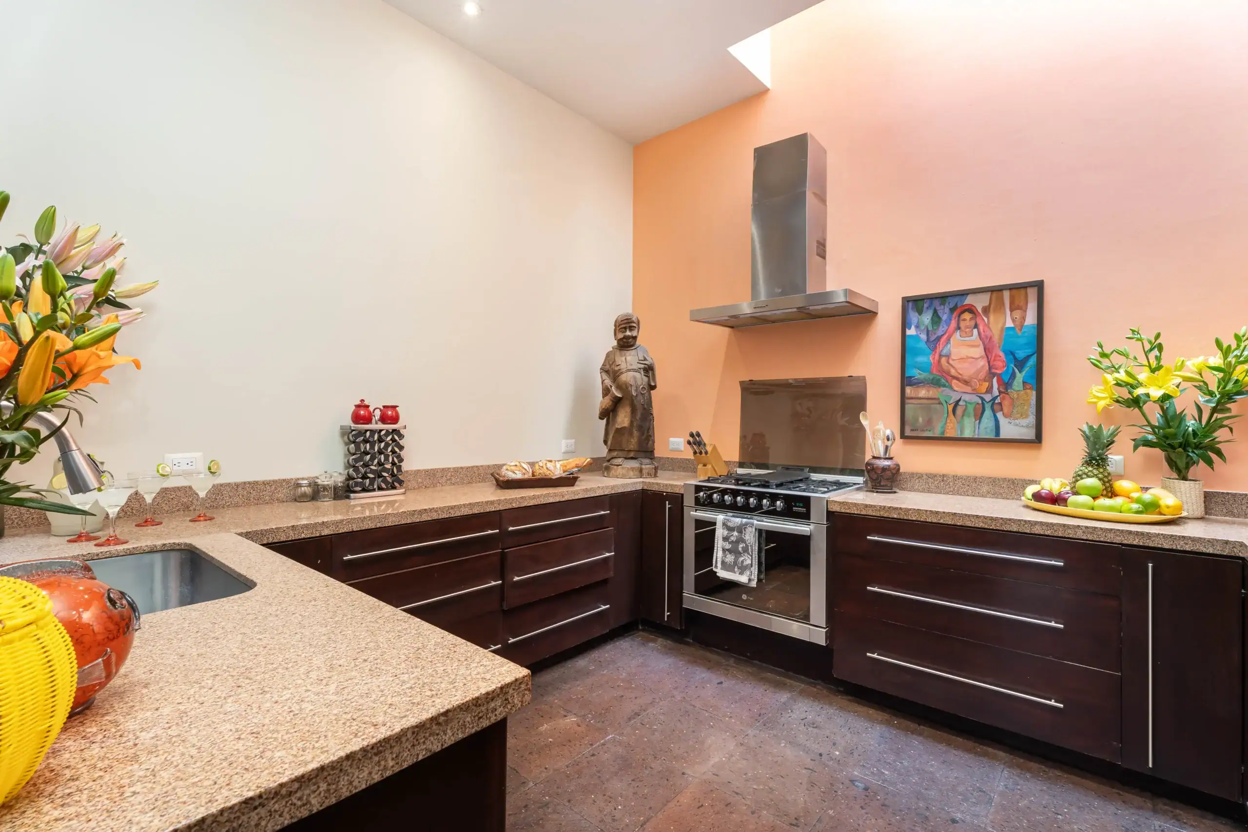 Kitchen with a peach accent wall, stainless range hood, dark wood cabinets, and a fruit bowl on the counter, San Miguel de Allende