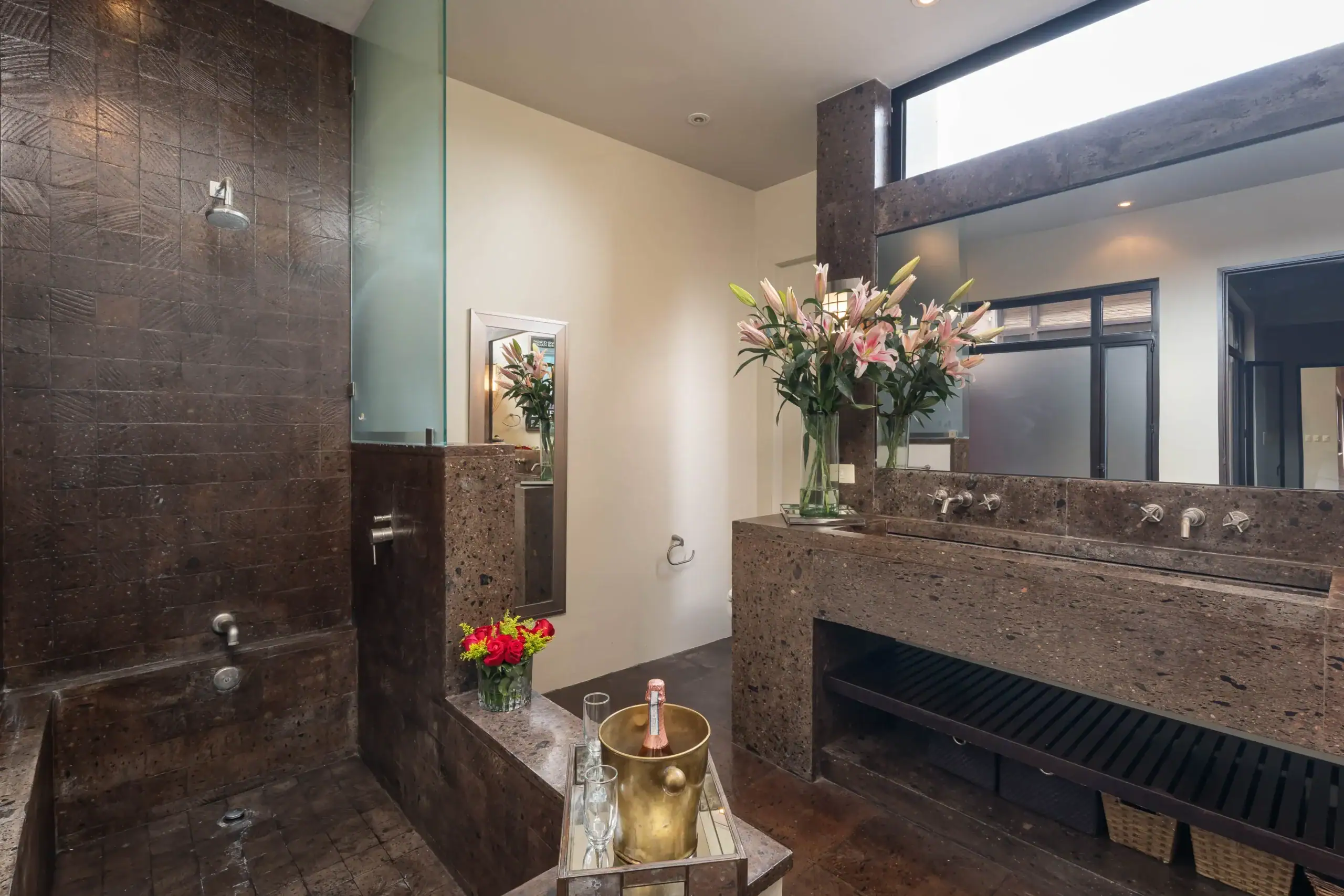 Luxurious bathroom with dark granite surfaces, a glass shower, and a vase of pink lilies on the counter, San Miguel de Allende