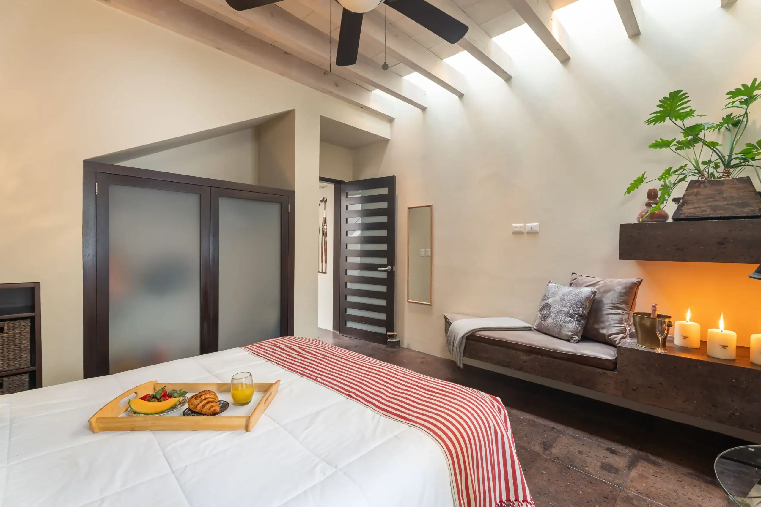 Breakfast tray on a white bed with croissants, fruit, and orange juice in a bright modern bedroom, San Miguel de Allende