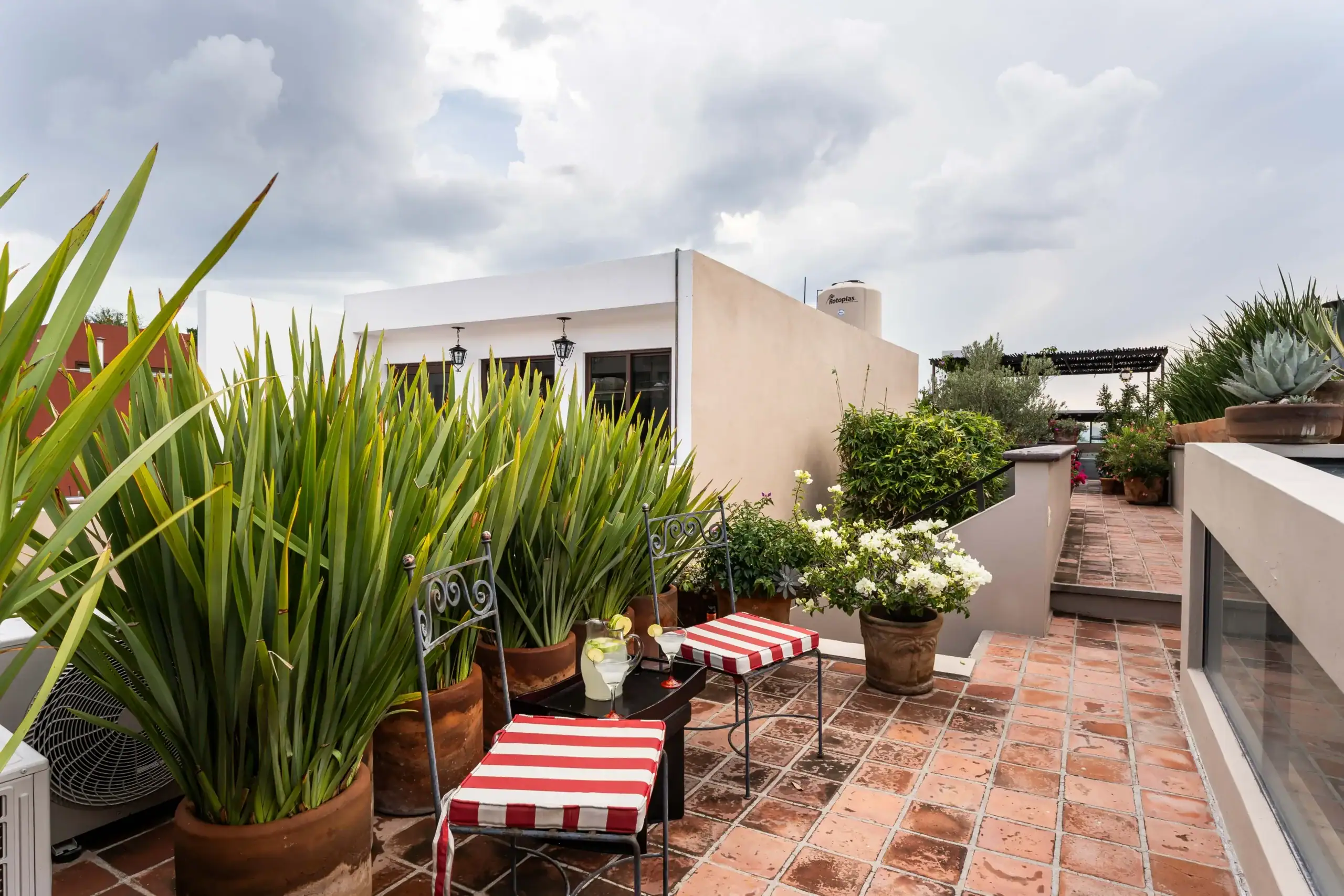 Roof terrace with red-and-white striped chairs, potted plants, and a beige building against a cloudy sky, San Miguel de Allende