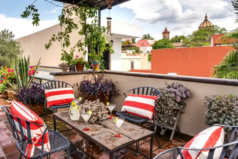 Rooftop patio with red-and-white striped cushions, metal chairs, and a table with drinks, surrounded by potted plants and a cityscape in the background, San Miguel de Allende