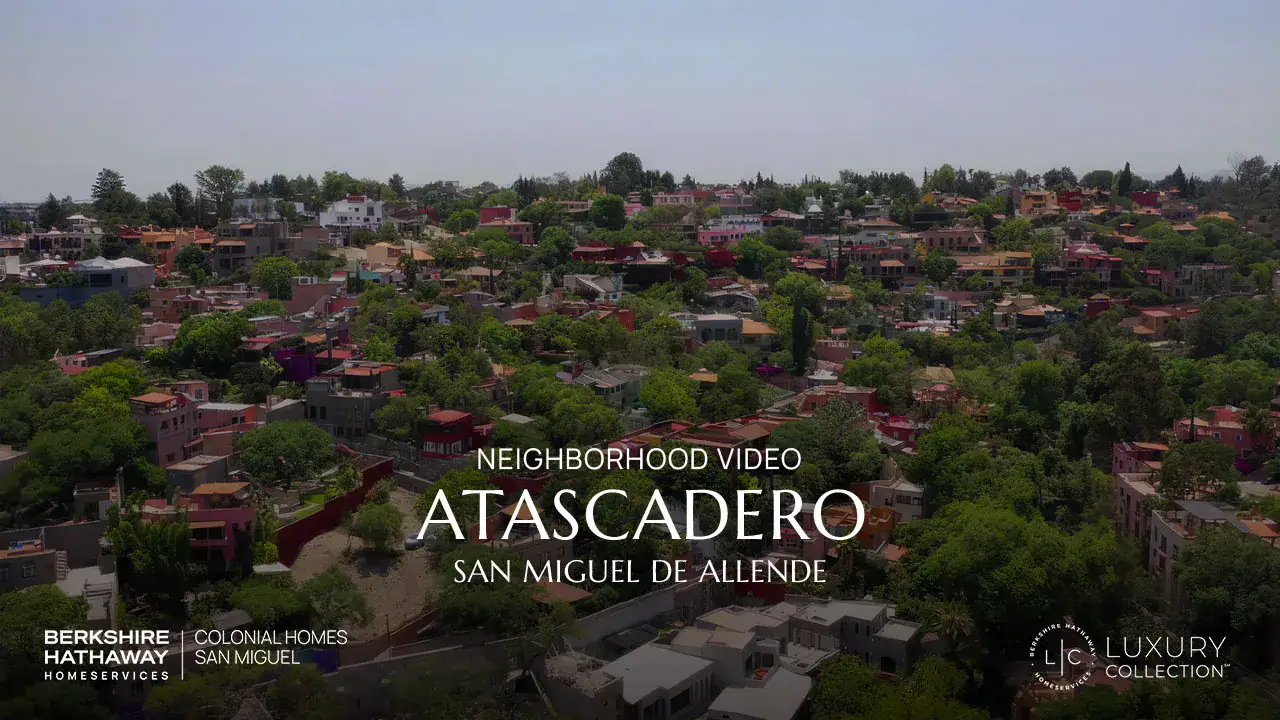 Aerial view of a colorful hillside neighborhood in San Miguel de Allende with the overlaid title 'NEIGHBORHOOD VIDEO ATASCADERO SAN MIGUEL DE ALLENDE' and logos in the corners for Berkshire Hathaway HomeServices and Luxury Collection.