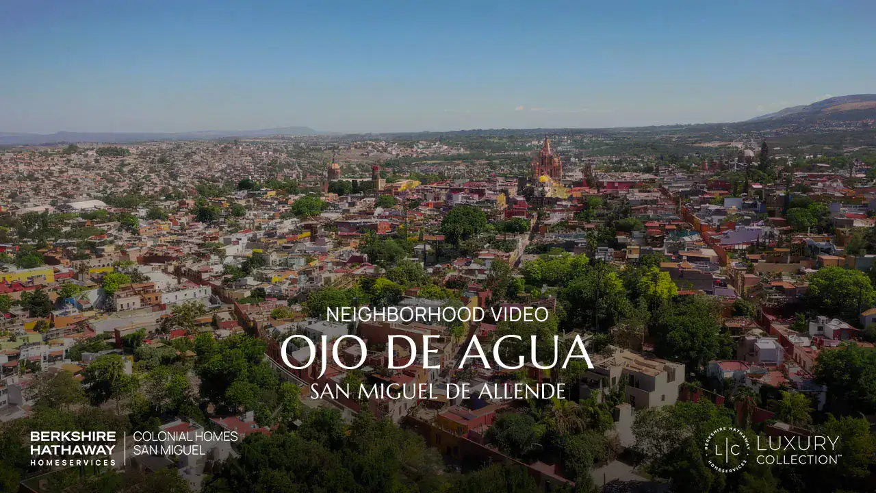 Aerial view of a colorful San Miguel de Allende neighborhood with overlaid title 'Ojo de Agua' and sponsor logos at the bottom left and right.