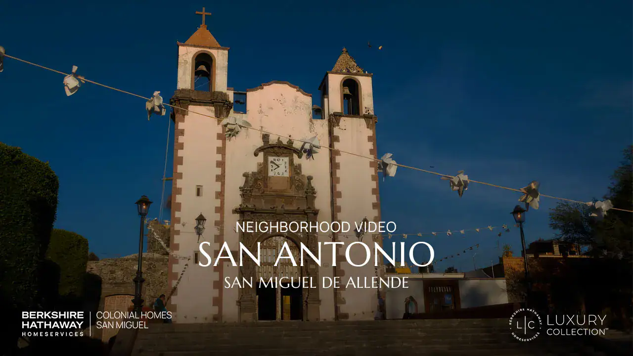 Church with two bell towers in San Miguel de Allende at dusk, string lights across the scene; overlay reads 'Neighborhood Video: San Antonio'.