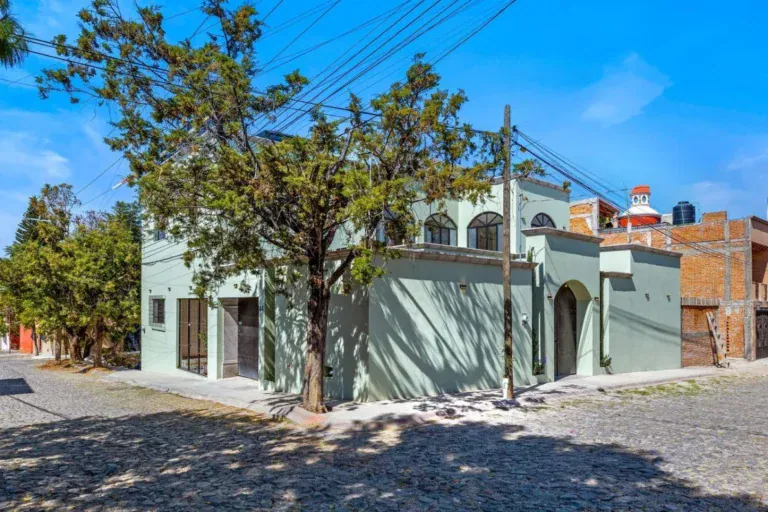 Casas Angel & Angelito, pale green house on a cobblestone corner with a tree, San Miguel de Allende