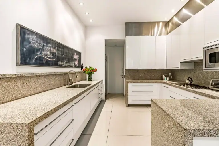 Bright modern kitchen with white cabinets, speckled granite countertops, and a chalkboard wall on the left; stainless steel sink and a vase of flowers on the counter, San Miguel de Allende