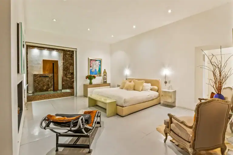 Bright modern bedroom with a large bed, tan headboard, and matching nightstands; decorative chairs and a lounge area visible, San Miguel de Allende