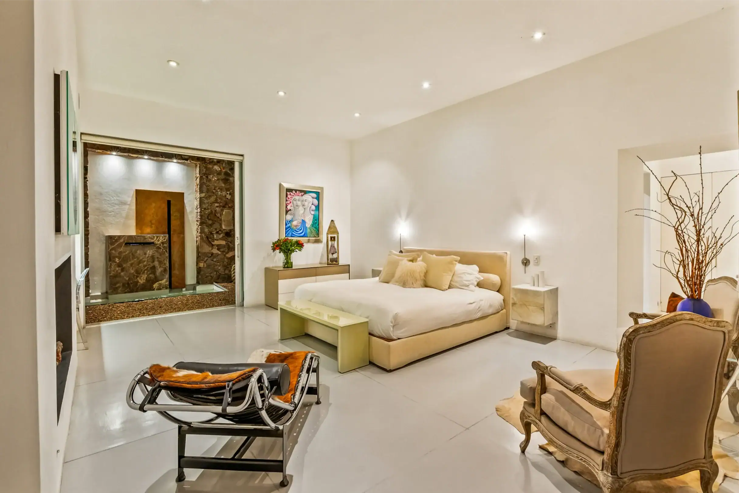 Bright modern bedroom with a large bed, tan headboard, and matching nightstands; decorative chairs and a lounge area visible, San Miguel de Allende
