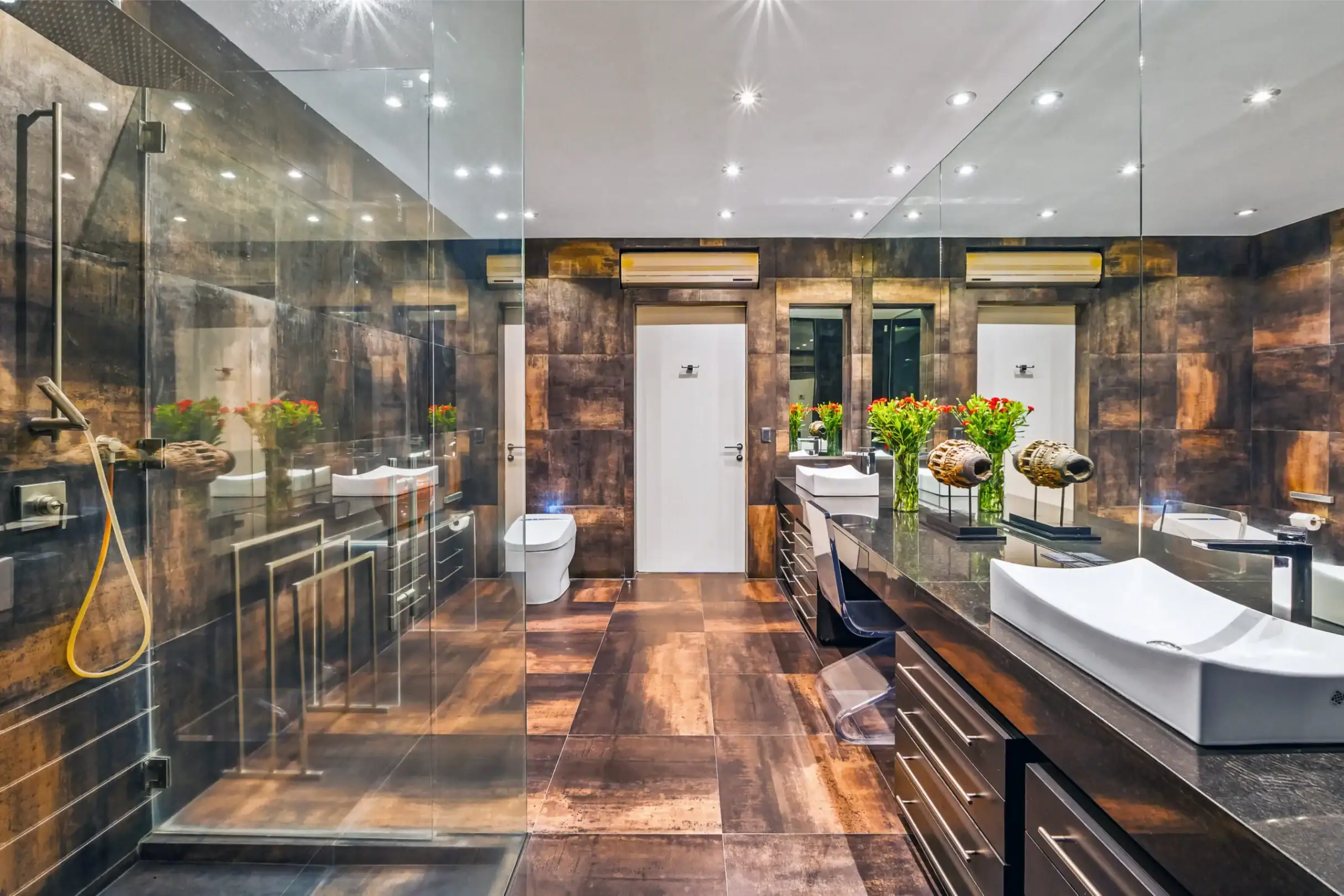 Modern bathroom with a glass shower enclosure, dark brown tiles, and a double vanity with red flowers on the counter, San Miguel de Allende