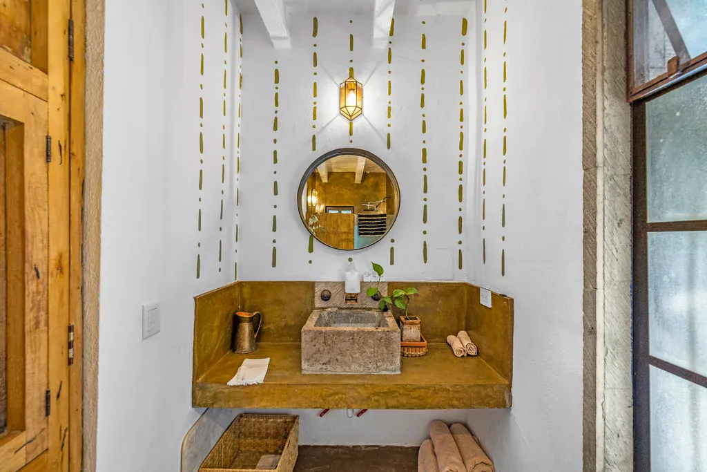 Casa Clae, bathroom with a stone sink, round mirror and a warm yellow counter, San Miguel de Allende