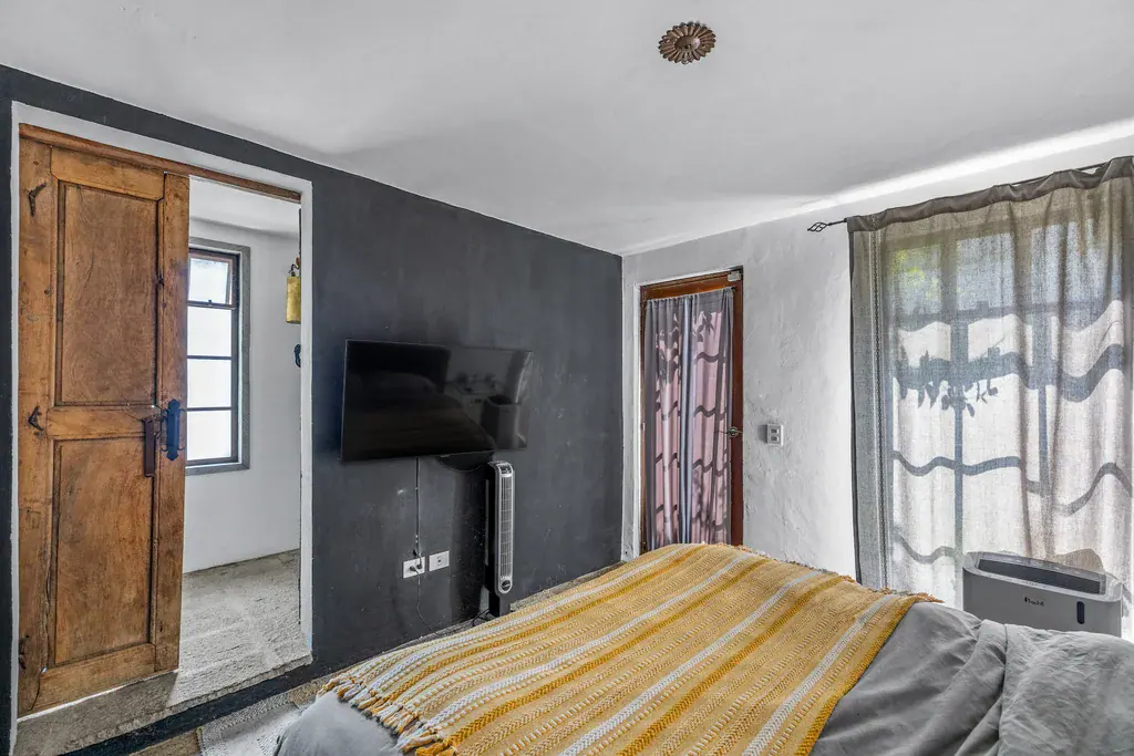 Casa Clae, bedroom with a wall-mounted television and a yellow striped throw, San Miguel de Allende