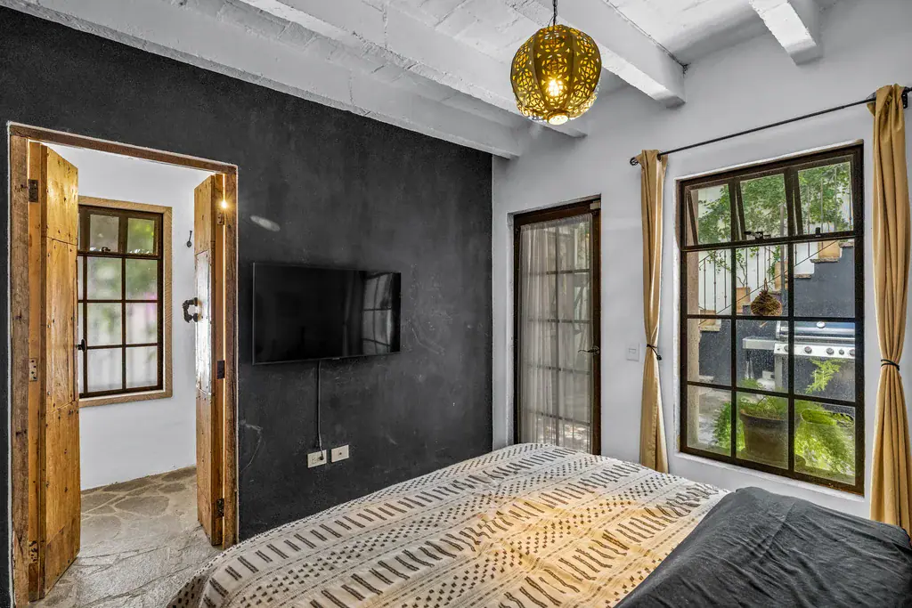 Casa Clae, bedroom with a patterned bedspread, wall-mounted television and a brass pendant lamp, San Miguel de Allende