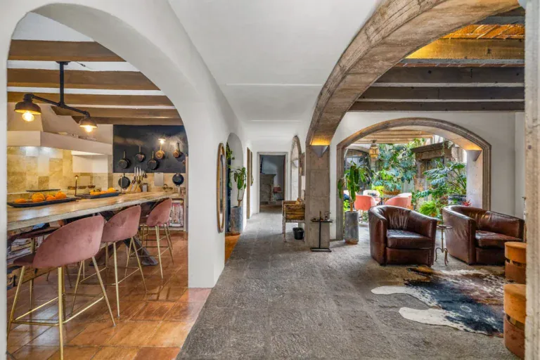 Casa Clae, kitchen island with pink bar stools and a stone arch toward the living room, San Miguel de Allende