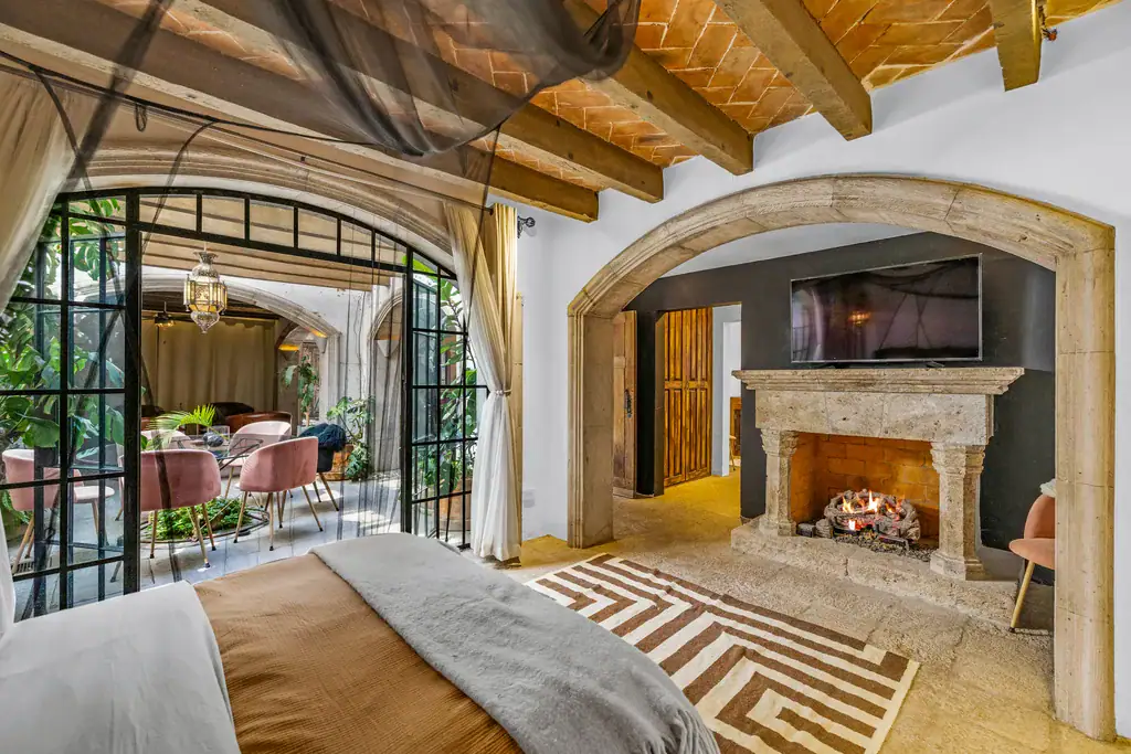 Casa Clae, bedroom with a stone fireplace and an arched doorway into the garden room, San Miguel de Allende