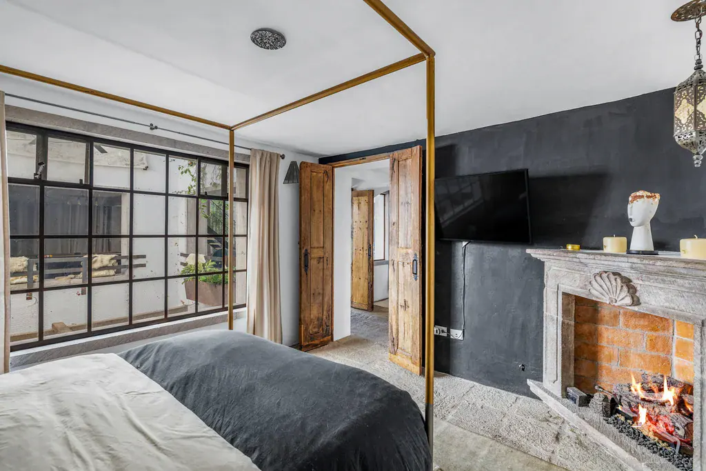 Casa Clae, bedroom with a four-poster bed, a stone fireplace and steel-framed windows, San Miguel de Allende
